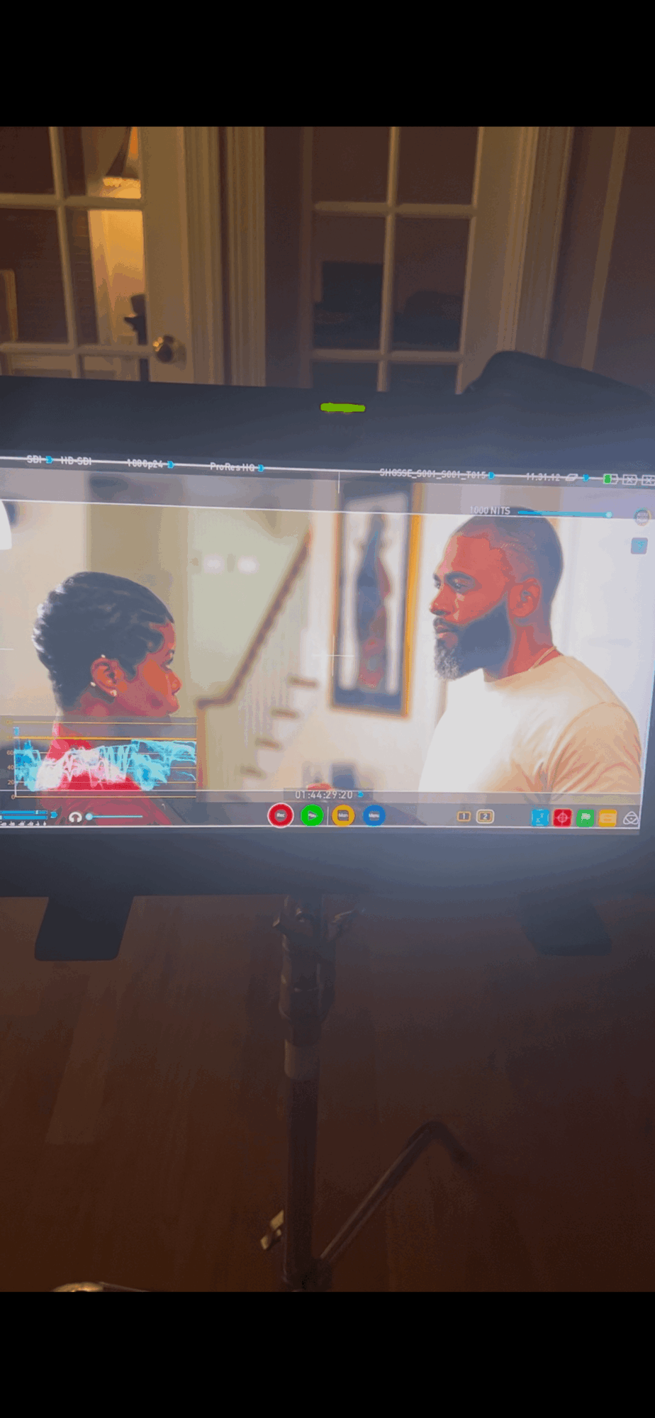 Two people face each other on a computer screen, one with curly hair and the other with a beard, in a room with windows.