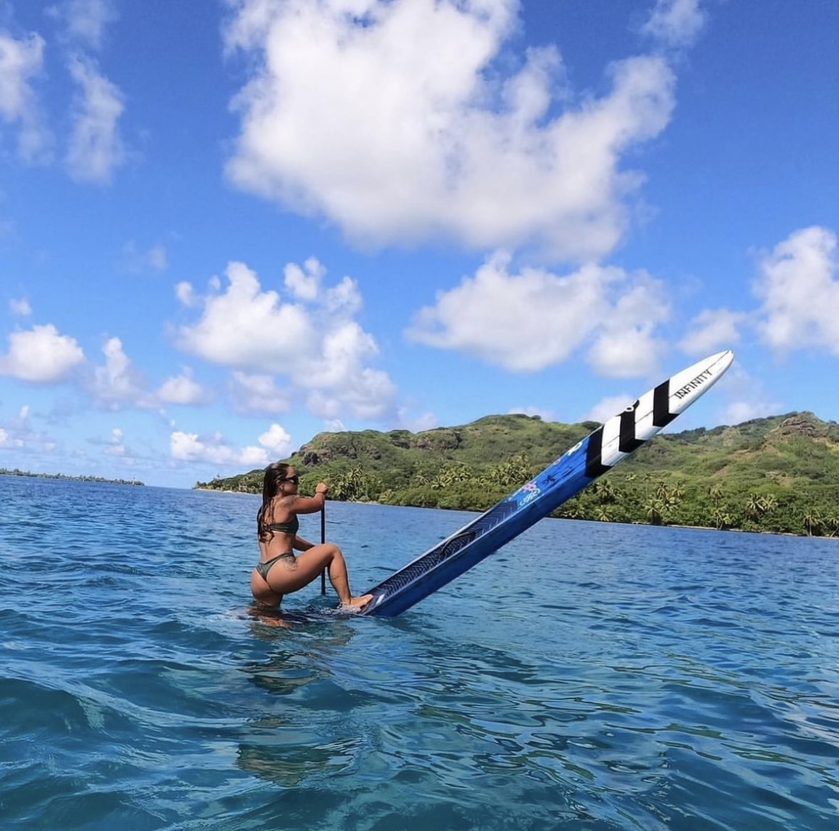 Person in water holding a large blue and white object, with a green island and blue sky in background.