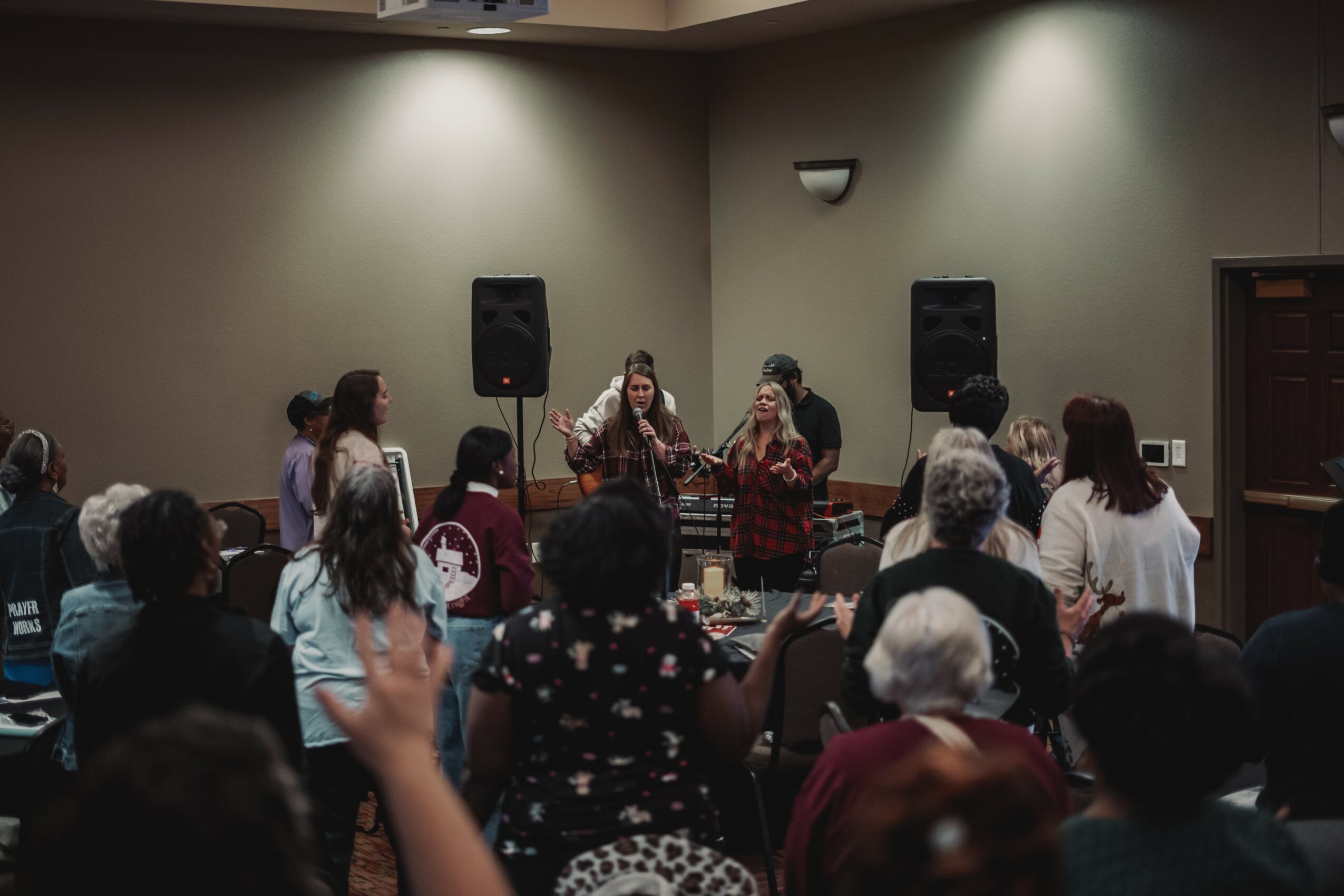 Group of people gathered in a room watching a live musical performance with two singers and instruments.