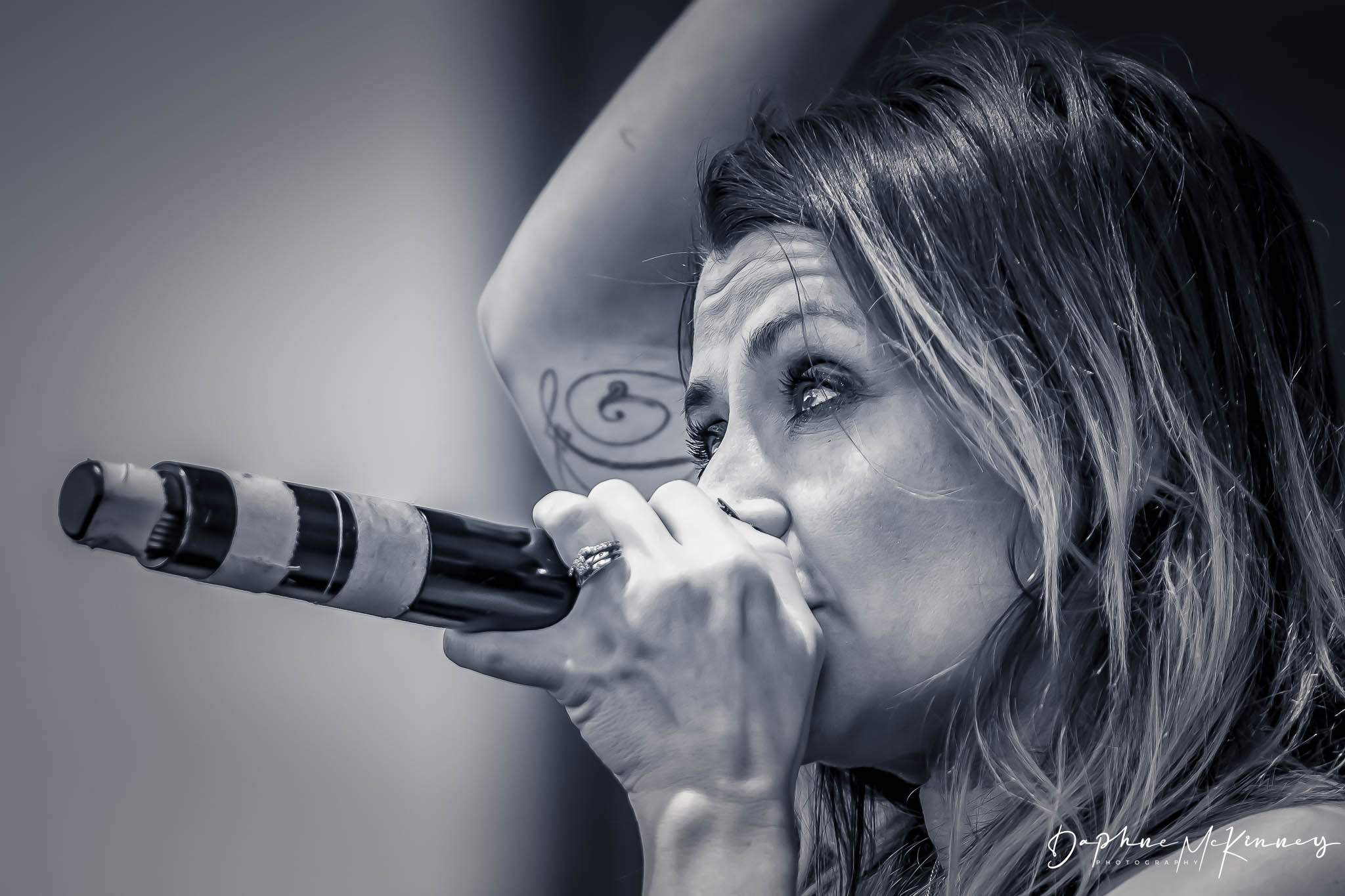 Woman singing into a microphone, with her arm raised, in black and white.