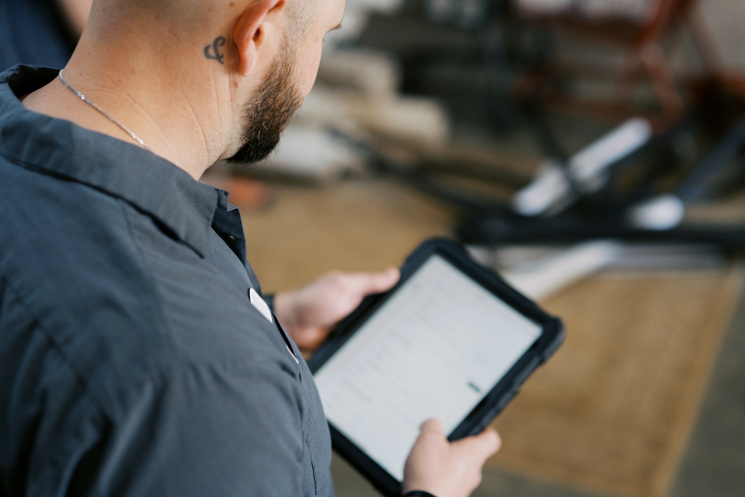 Person with short hair and a beard looking at a tablet, wearing a dark jacket, in an outdoor setting.