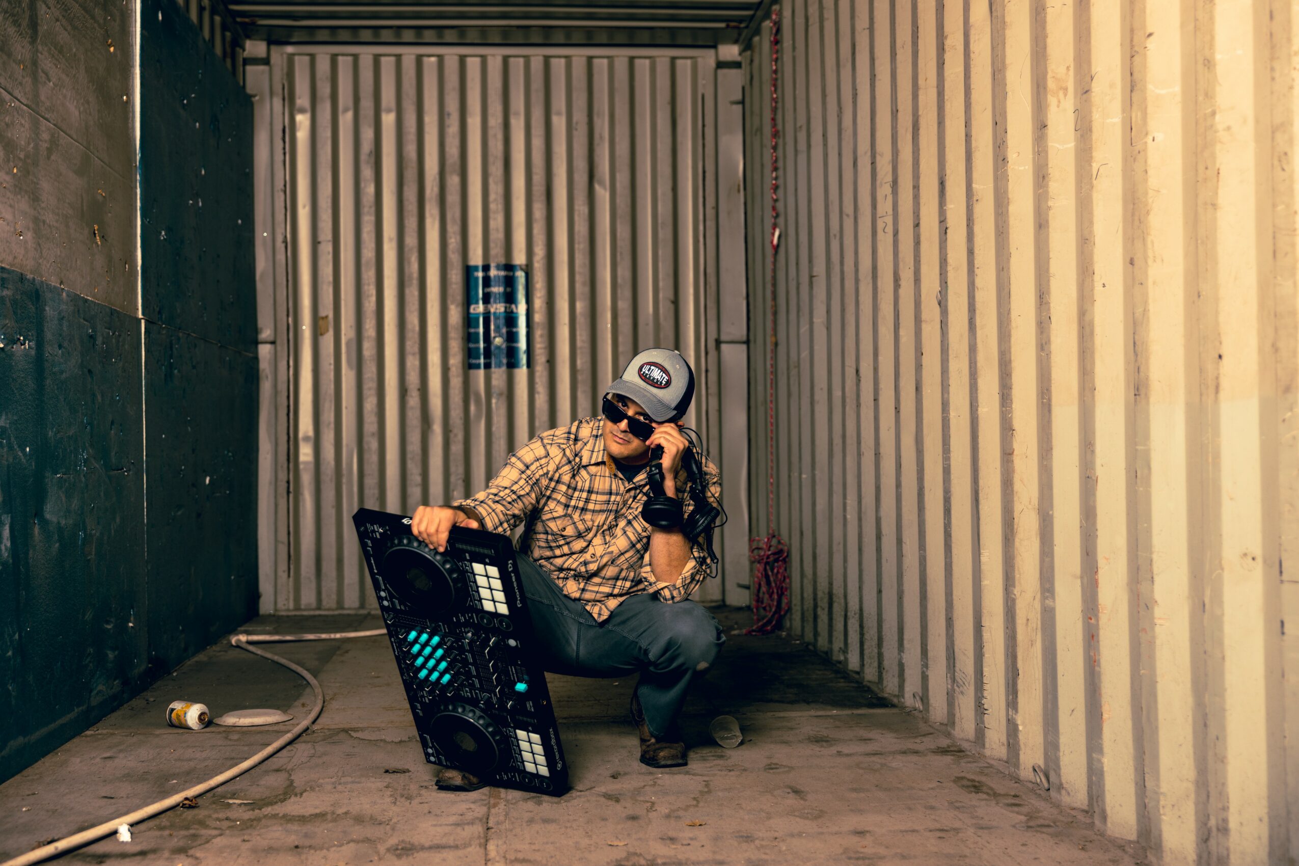 Person sitting on the ground in a narrow alleyway, holding a phone, with a shopping basket nearby, walls on both sides.