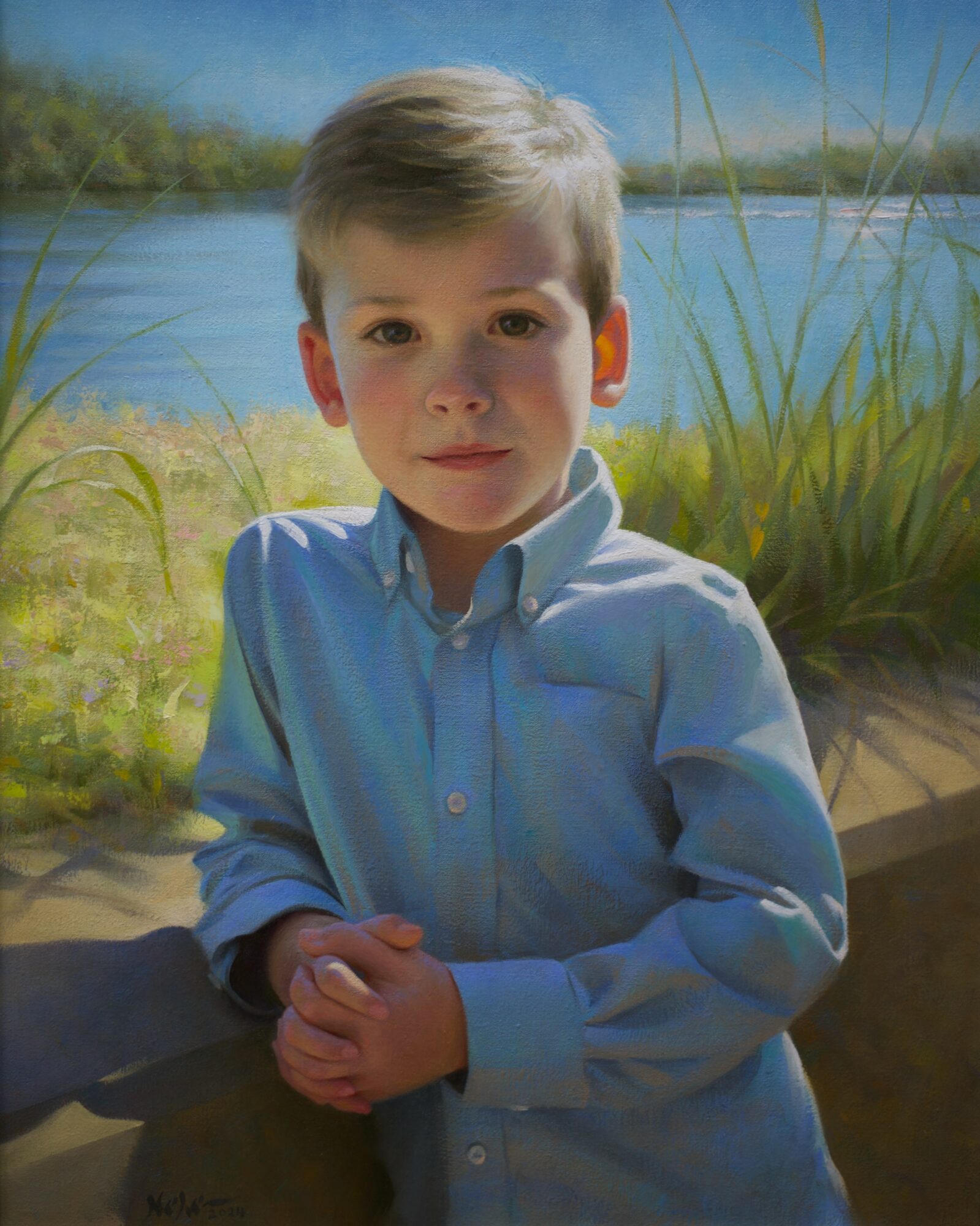 Young boy with short hair wearing a light blue shirt, standing outdoors near water and grass, looking at the camera.