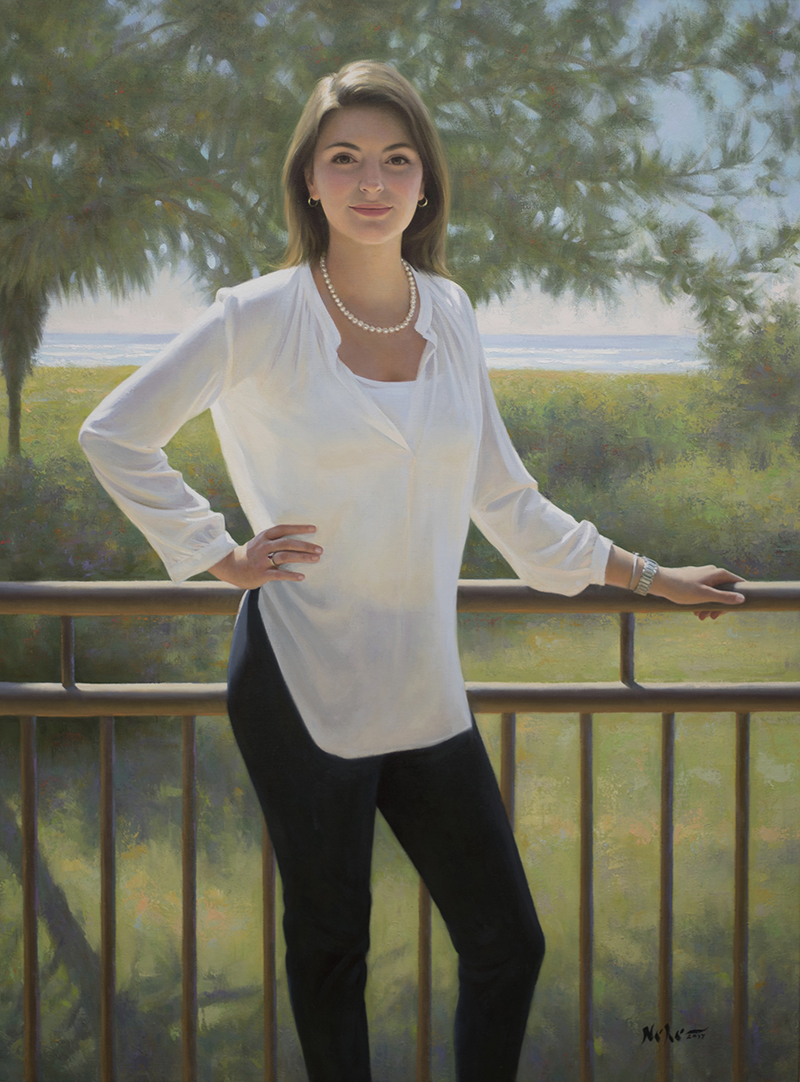 Woman standing outdoors with trees and a railing, wearing a white blouse and black pants, smiling at the camera.