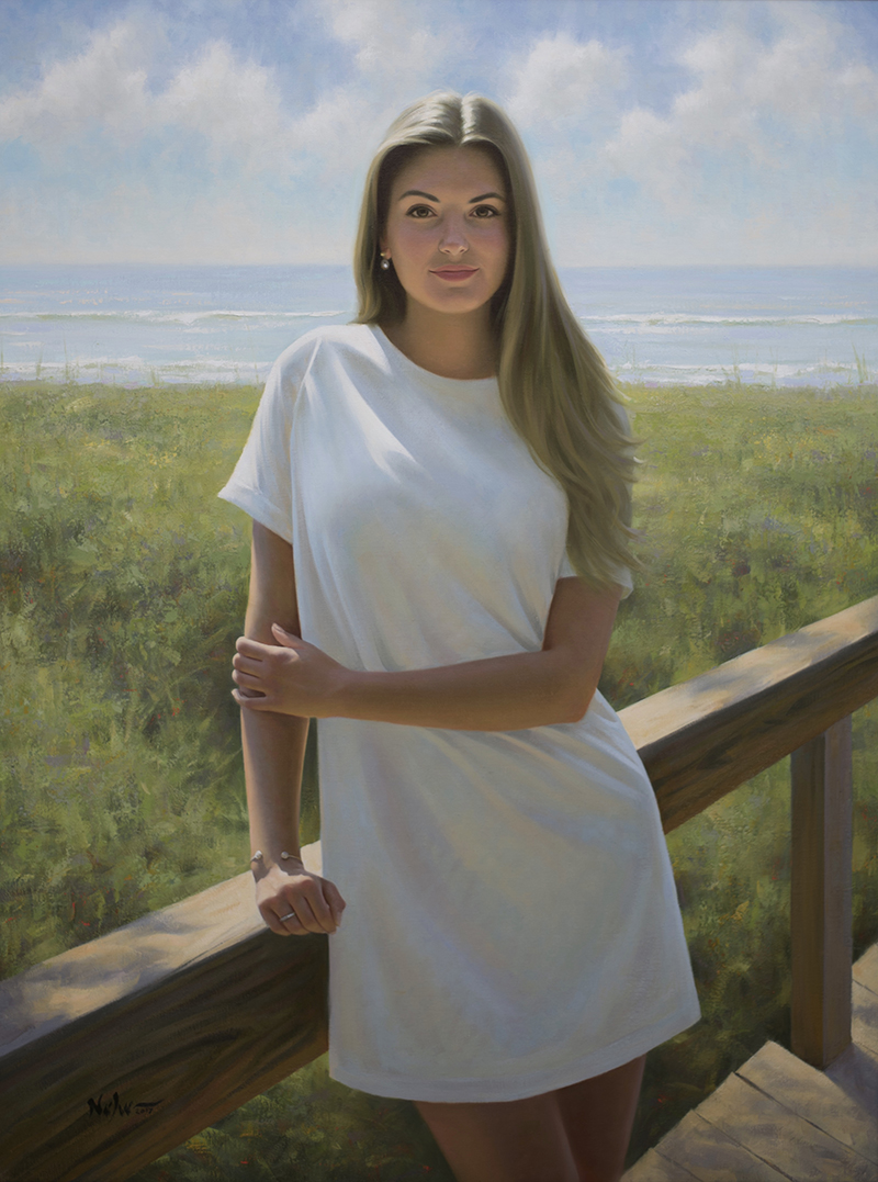 Young woman with long hair standing outdoors on a wooden deck, with a grassy area and ocean in the background.