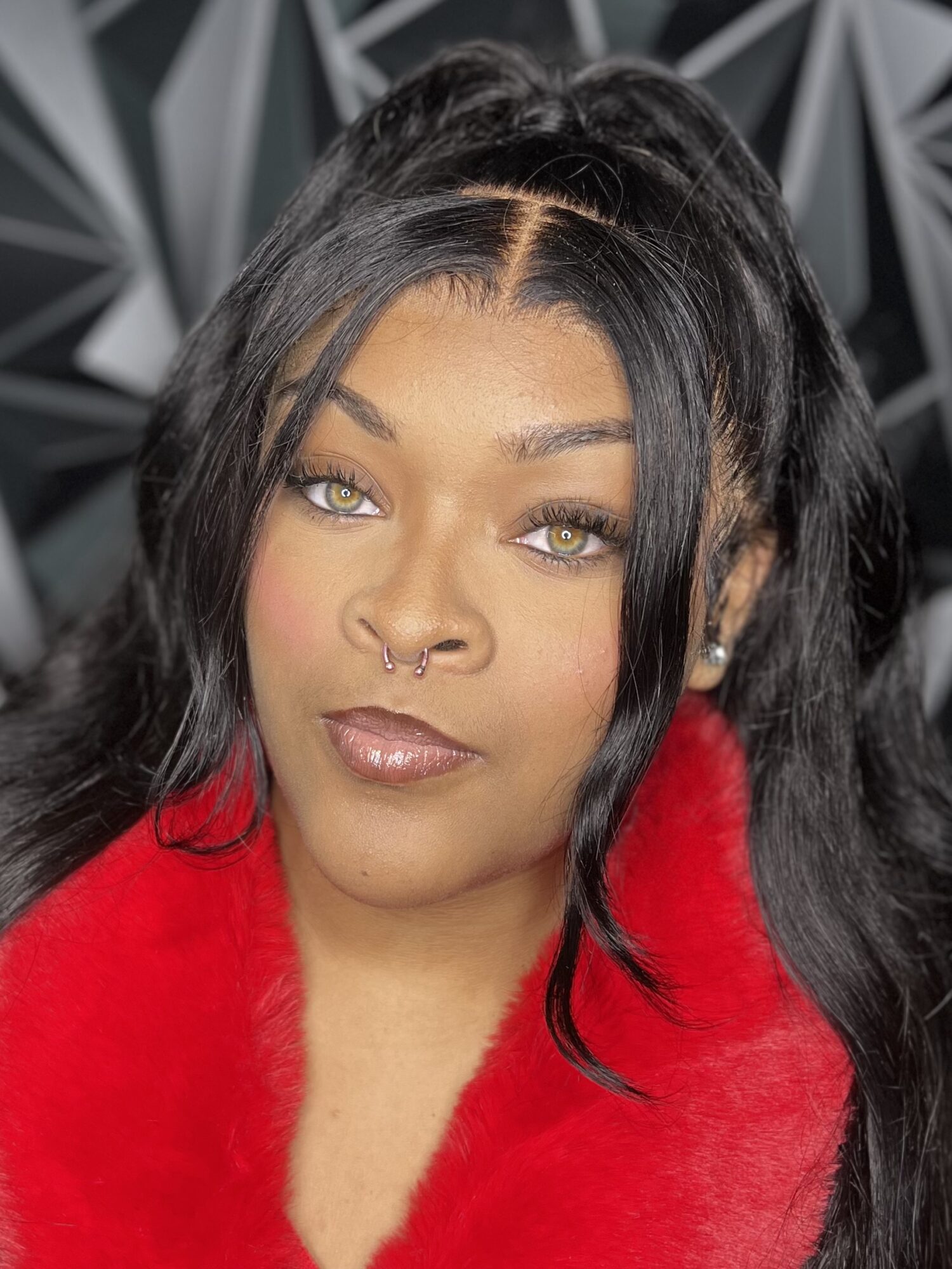 Woman with long black hair, green eyes, nose ring, wearing a red fur coat, looking at camera.