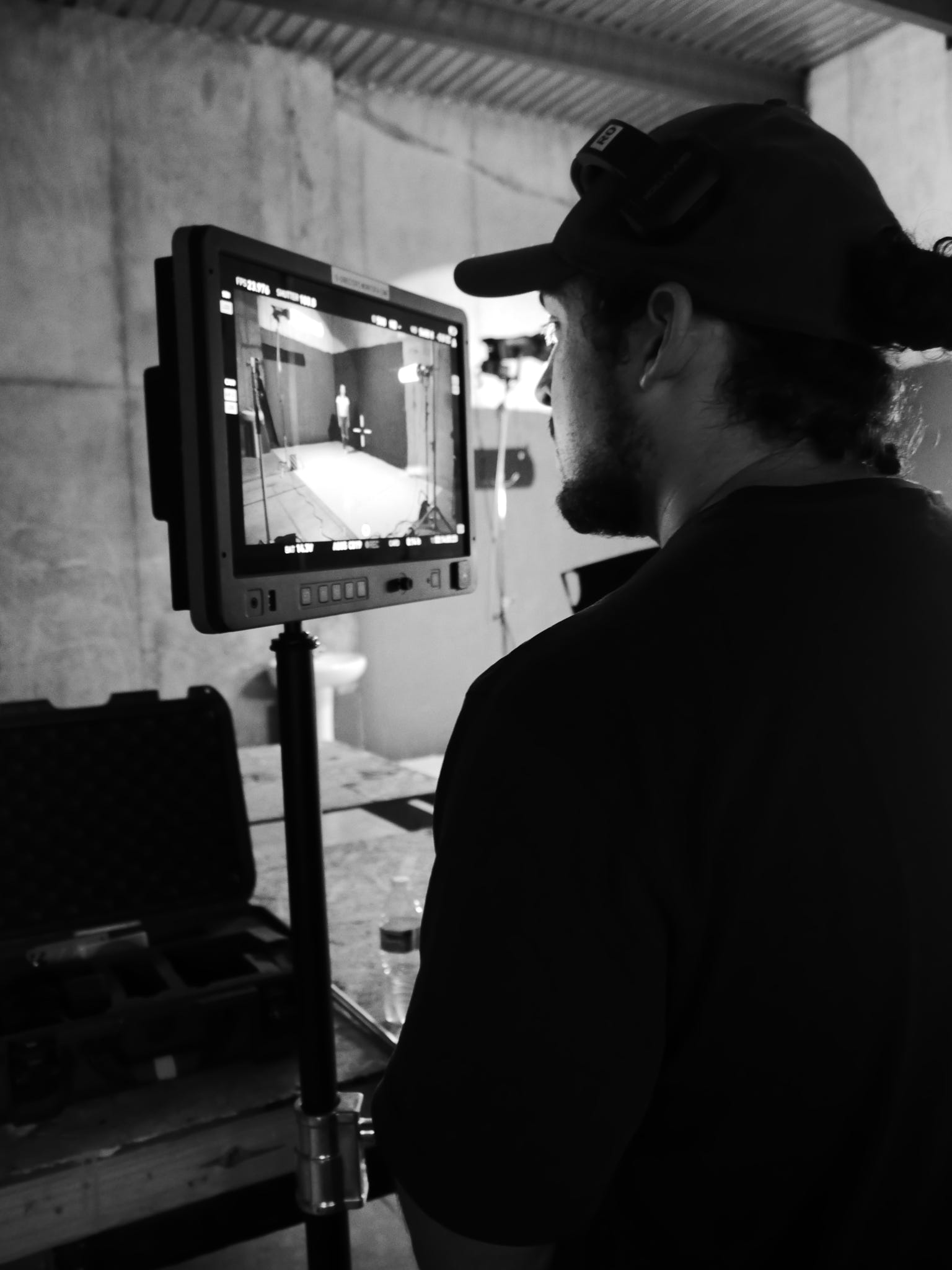 Person wearing a cap looks at a monitor on a stand in a room with concrete walls.