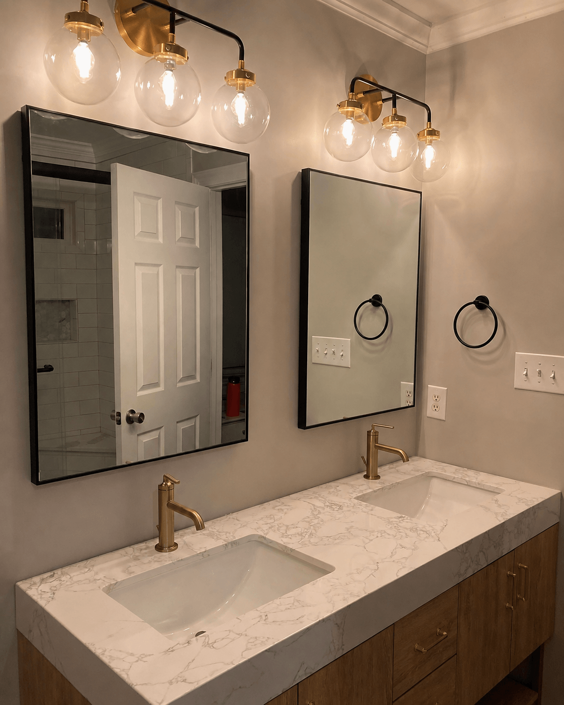 Double vanity with marble countertop, two sinks, gold faucets, mirrors, and wall-mounted light fixtures, in a bathroom.