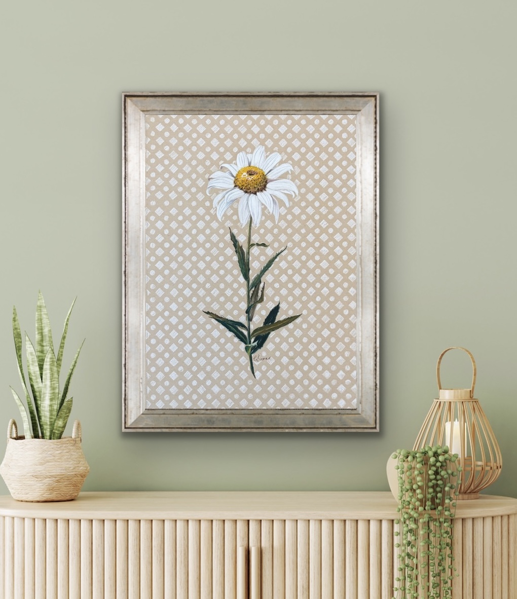 Framed botanical print of a daisy flower on a patterned background, hanging on a light green wall, with a plant and decorative items below.