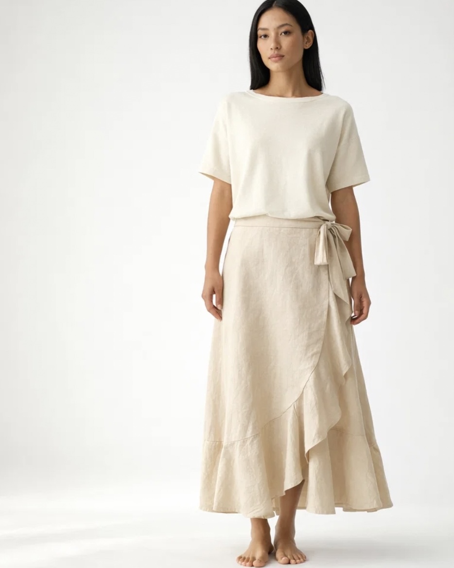 Woman in cream-colored top and long skirt with ruffle detail, standing barefoot against a plain background.