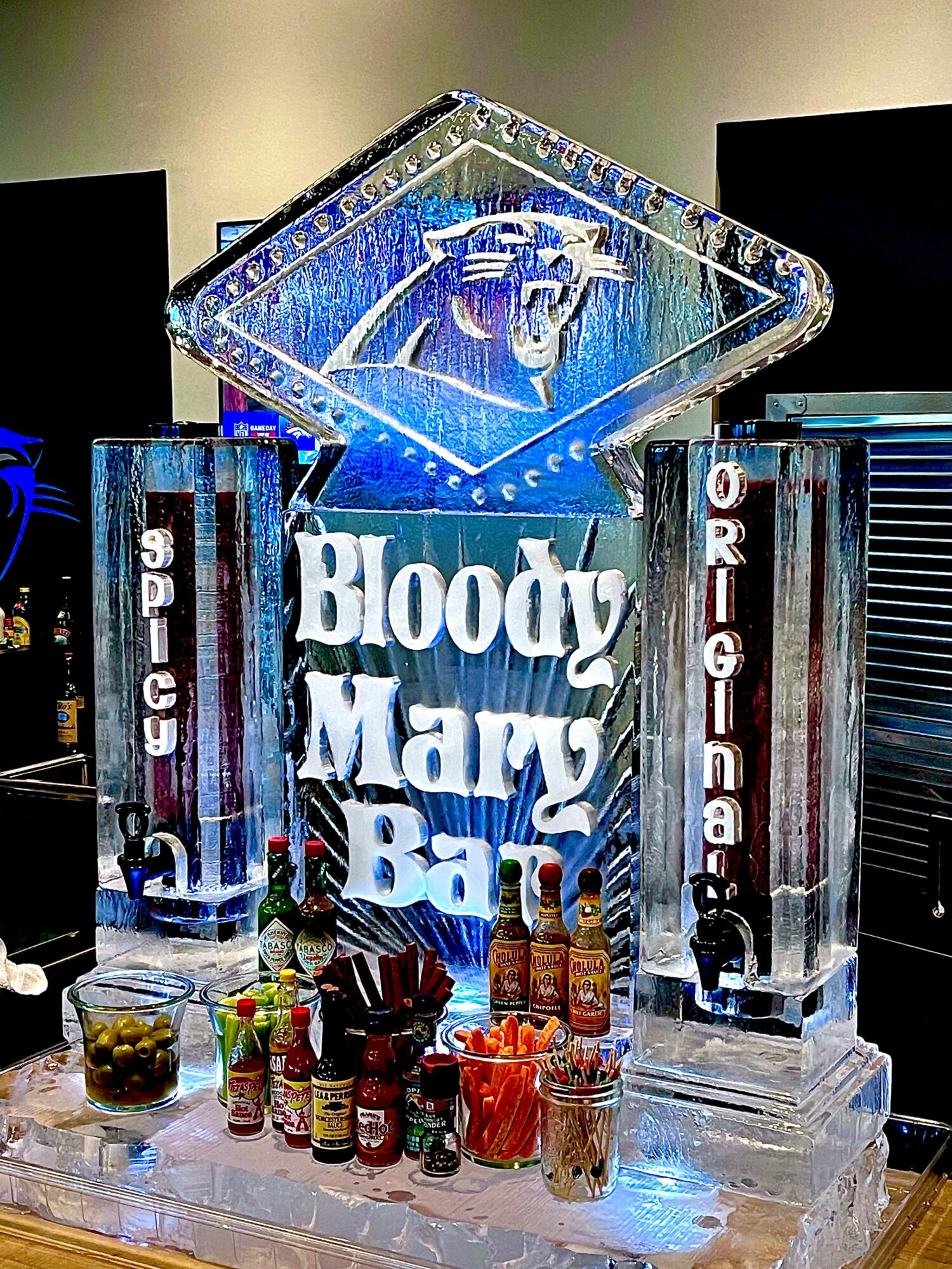 Ice sculpture with a bull's head, illuminated, with bottles and snacks in front, and text reading 'Bloody Mary Bar'.