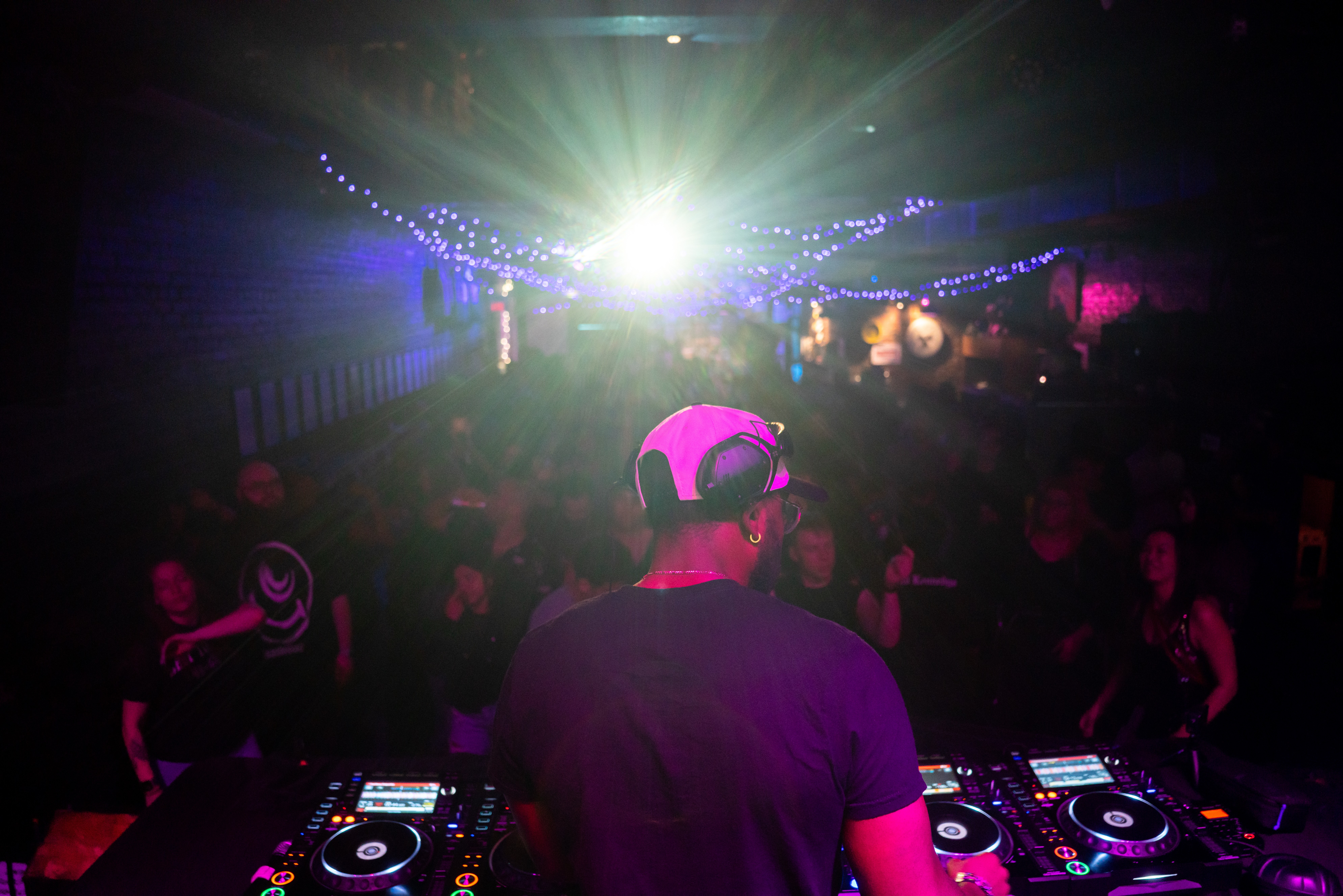DJ wearing headphones performs at a nightclub with colorful lights and a crowd dancing.