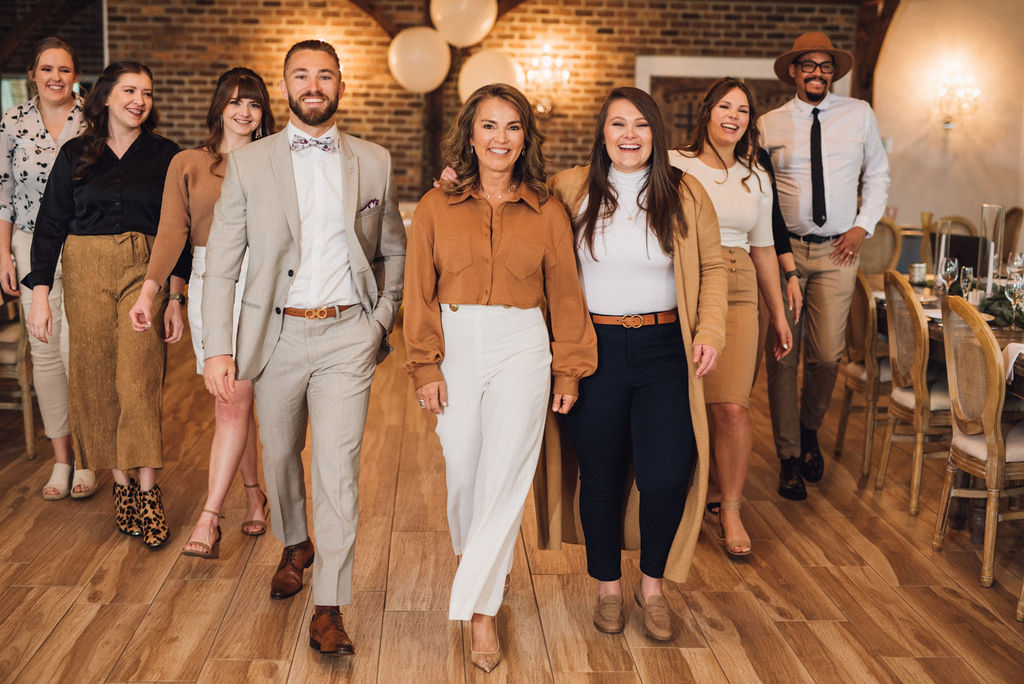 Group of nine diverse people walking in a decorated indoor space with brick walls and wooden floors.