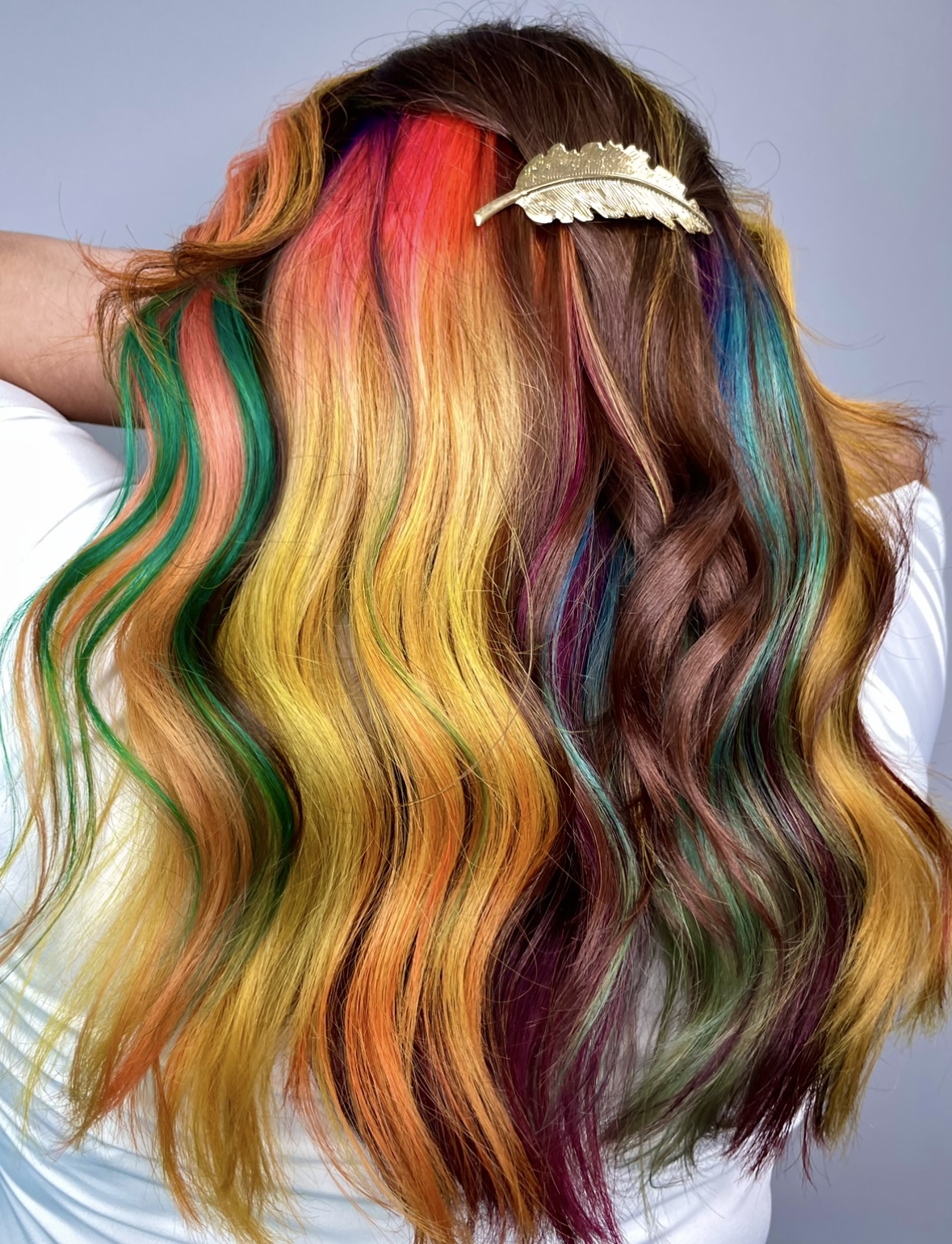 Person with long, wavy hair dyed in rainbow colors, including red, yellow, green, blue, and purple, with a hair clip.