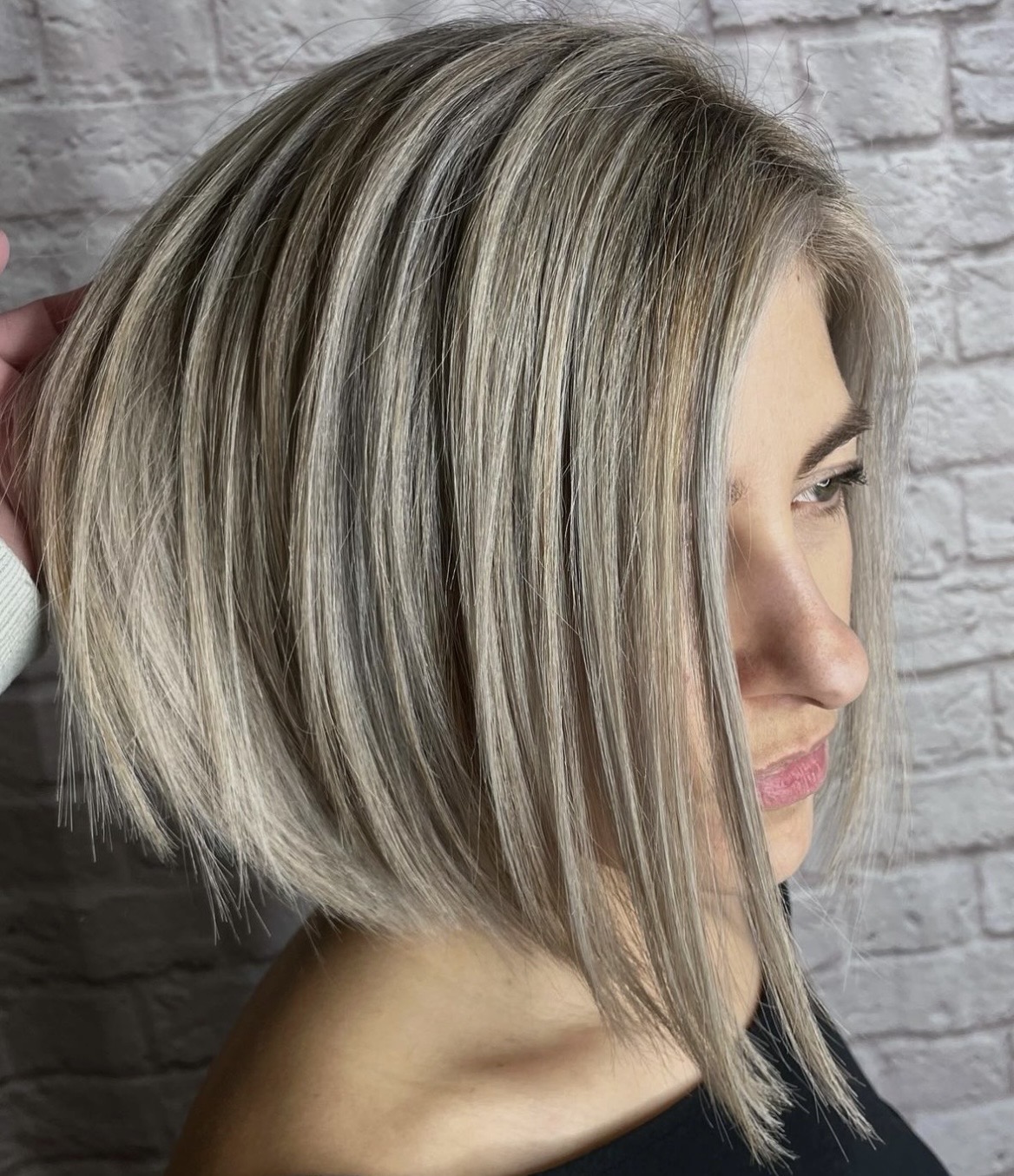 Side view of a woman with a short, straight, blonde bob hairstyle against a brick wall background.