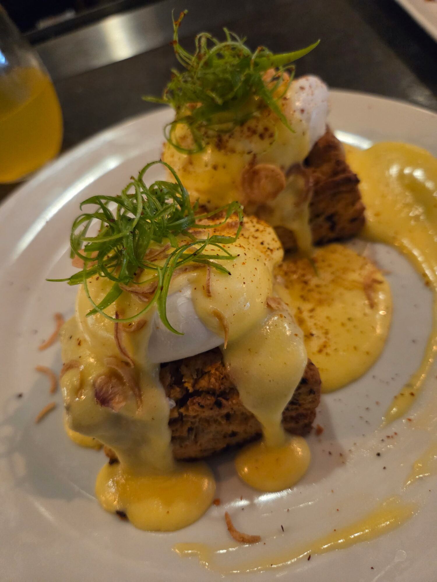 Dish with grilled meat, topped with poached eggs, green garnish, and creamy sauce on a white plate.