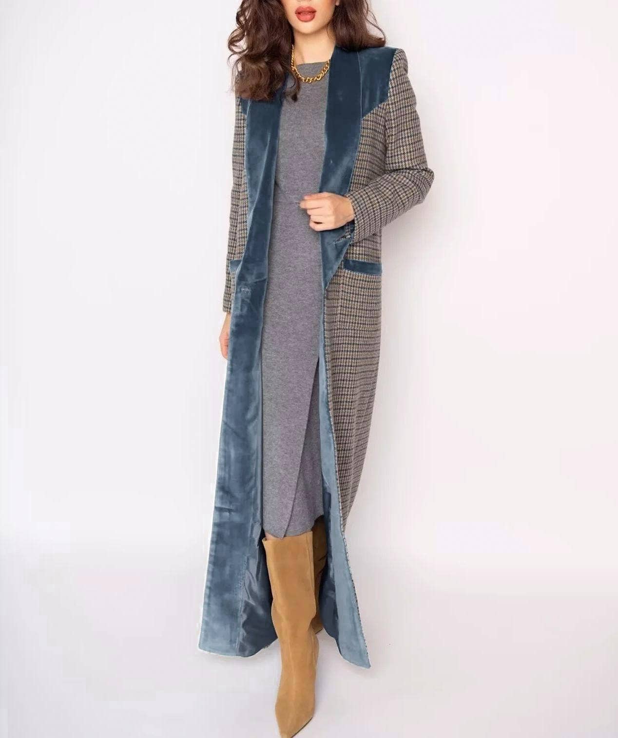 Woman in a long coat with checkered and denim sections, wearing a gray dress and tan boots, standing against a white background.