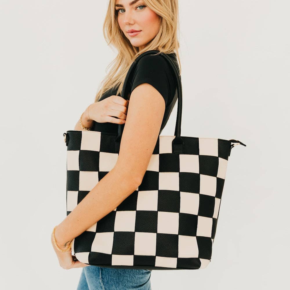 Woman with blonde hair holding a black and white checkered tote bag, wearing a black top, against a plain white background.