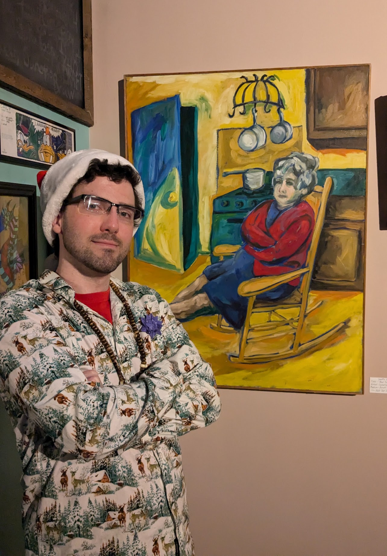 Man with glasses and a white hat stands with arms crossed in front of a colorful painting of a woman sitting in a chair.