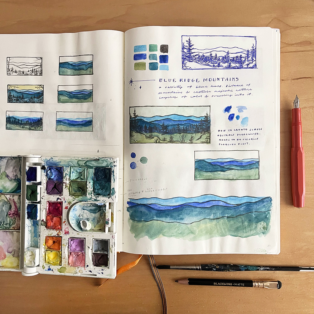 Open sketchbook with watercolor mountain studies, color swatches, and notes, on a wooden table with a red pen and watercolor palette.