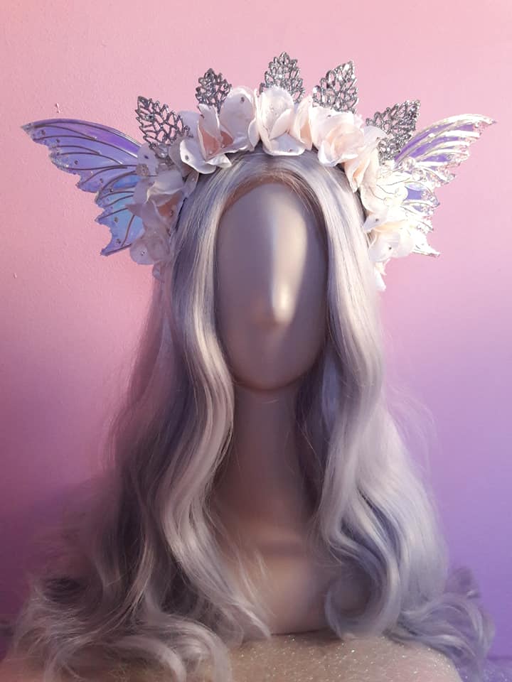 Headpiece with white flowers, silver butterflies, and purple butterfly wings on a mannequin with long, wavy, platinum blonde hair.