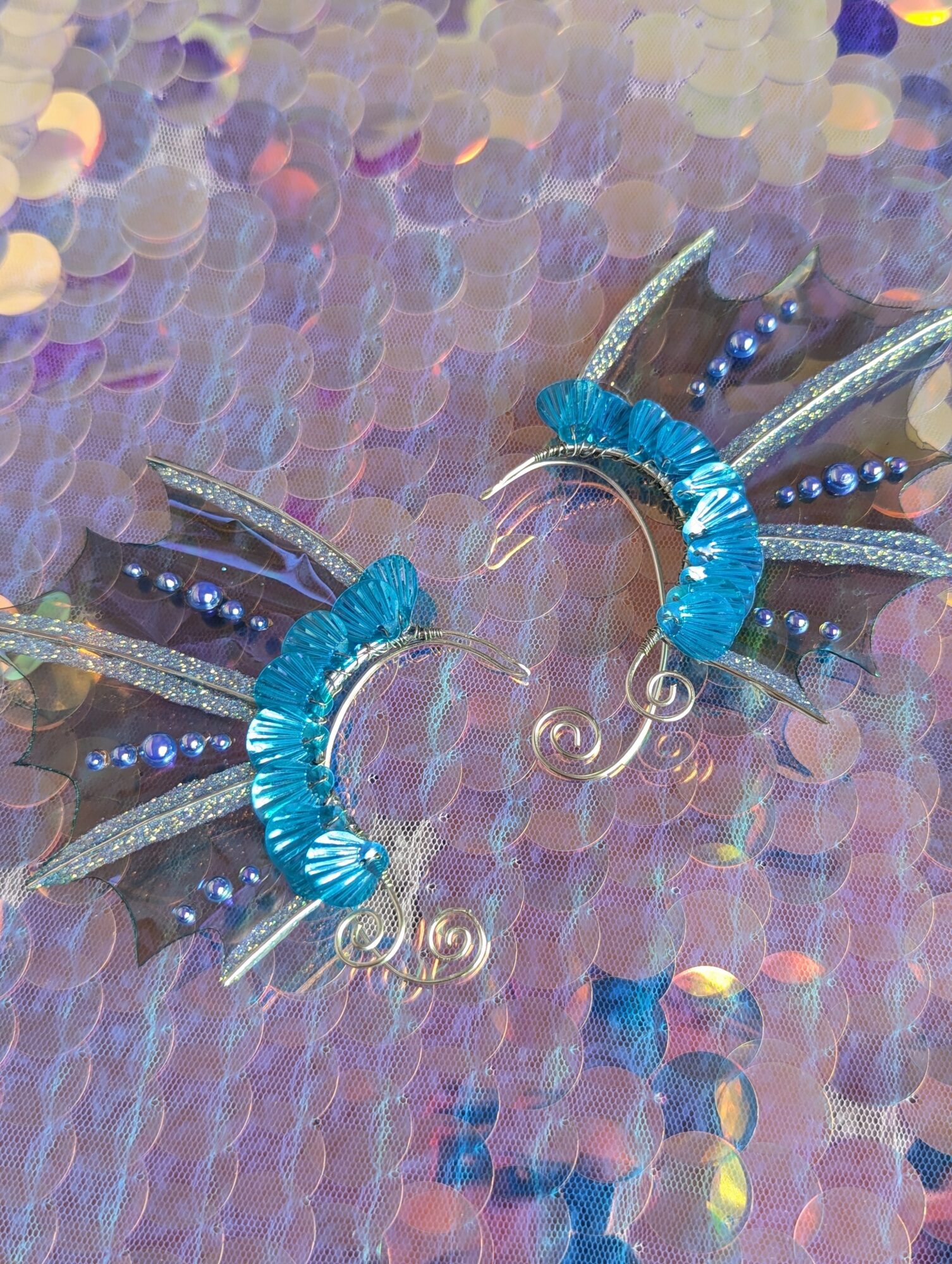 Decorative earrings with blue, silver, and black elements, placed on a colorful, iridescent background.