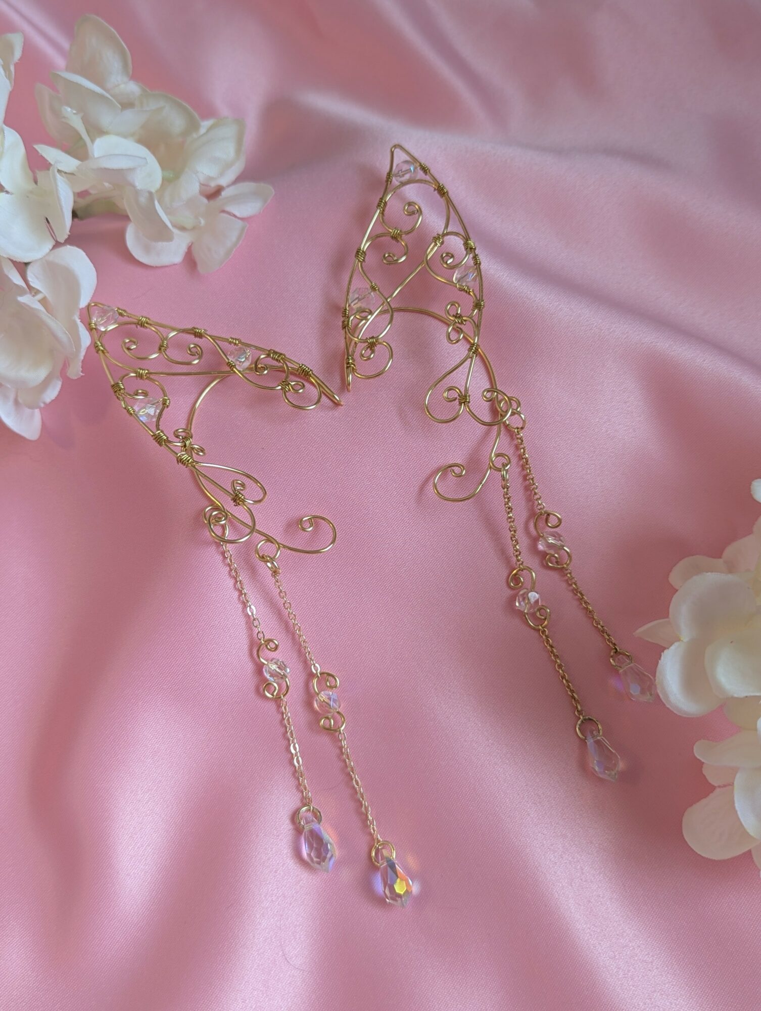 Gold decorative jewelry with dangling beads on pink satin fabric, surrounded by white flowers.