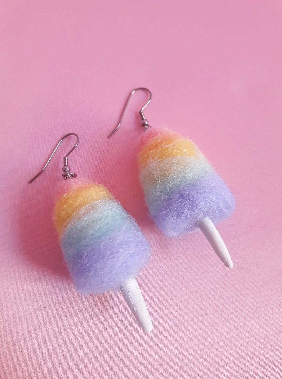 Colorful rainbow felt earrings with white cone-shaped dangles on pink background.