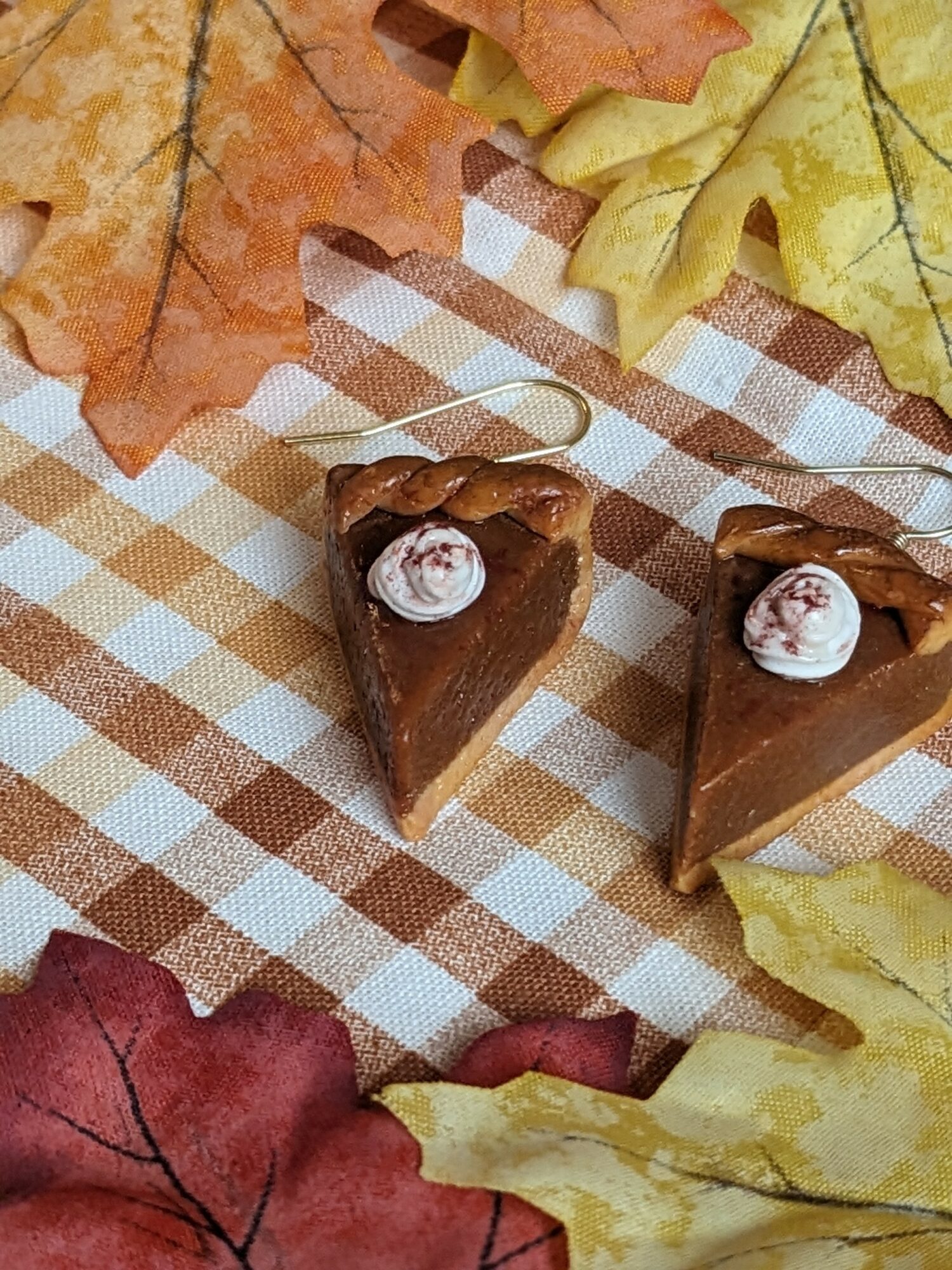 Two slices of chocolate cake with whipped cream and cherry topping on a checkered cloth, surrounded by autumn leaves.