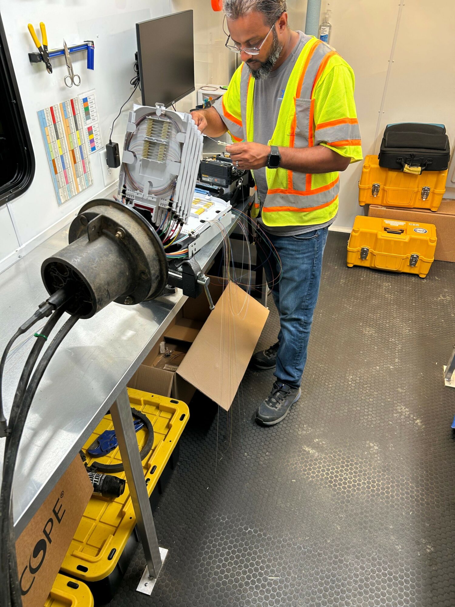 Person in safety vest working with machinery and tools on a workbench, with yellow toolboxes nearby.