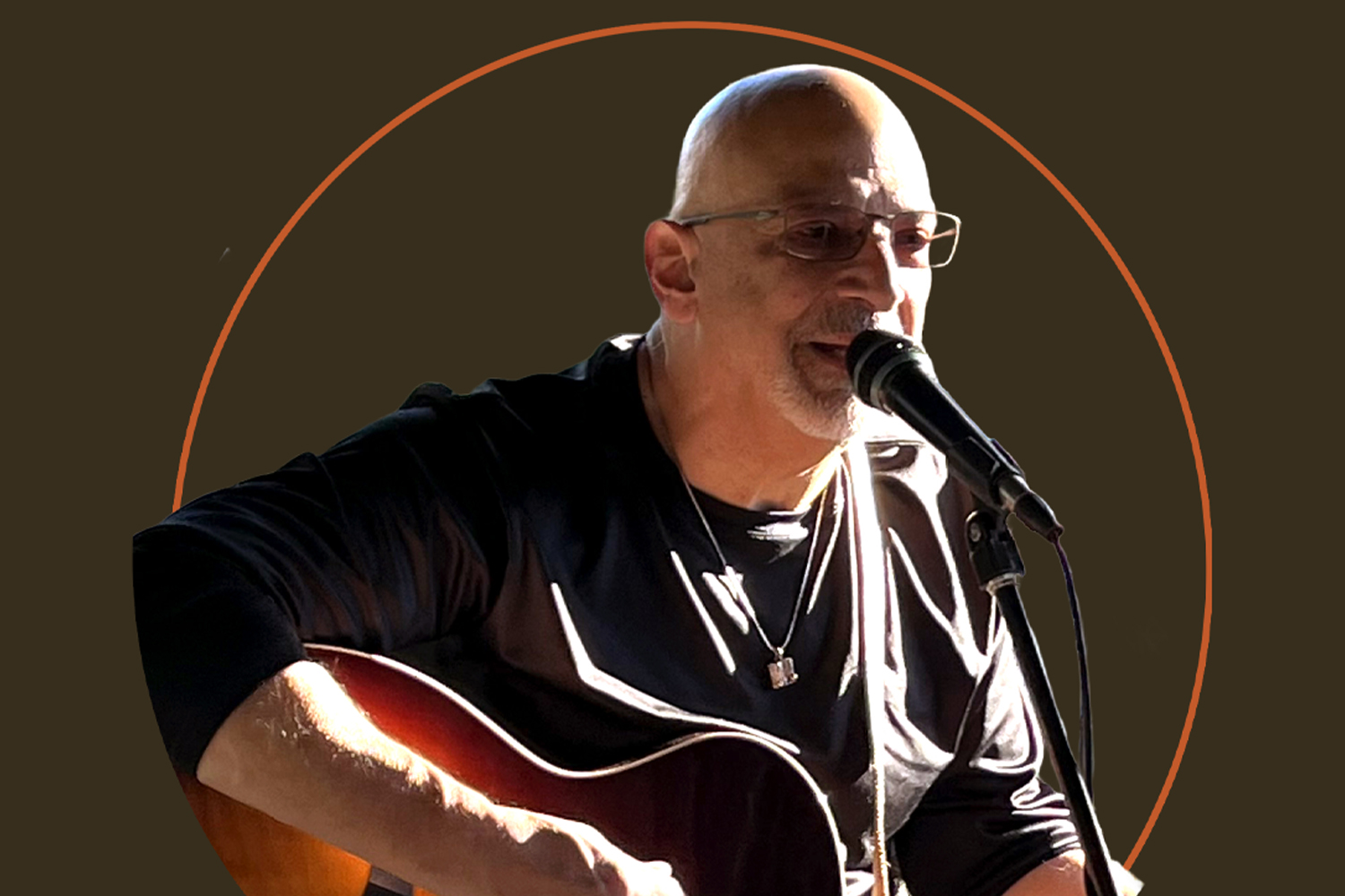 Bald man with glasses singing into a microphone while playing guitar, with a dark background and orange circle outline.