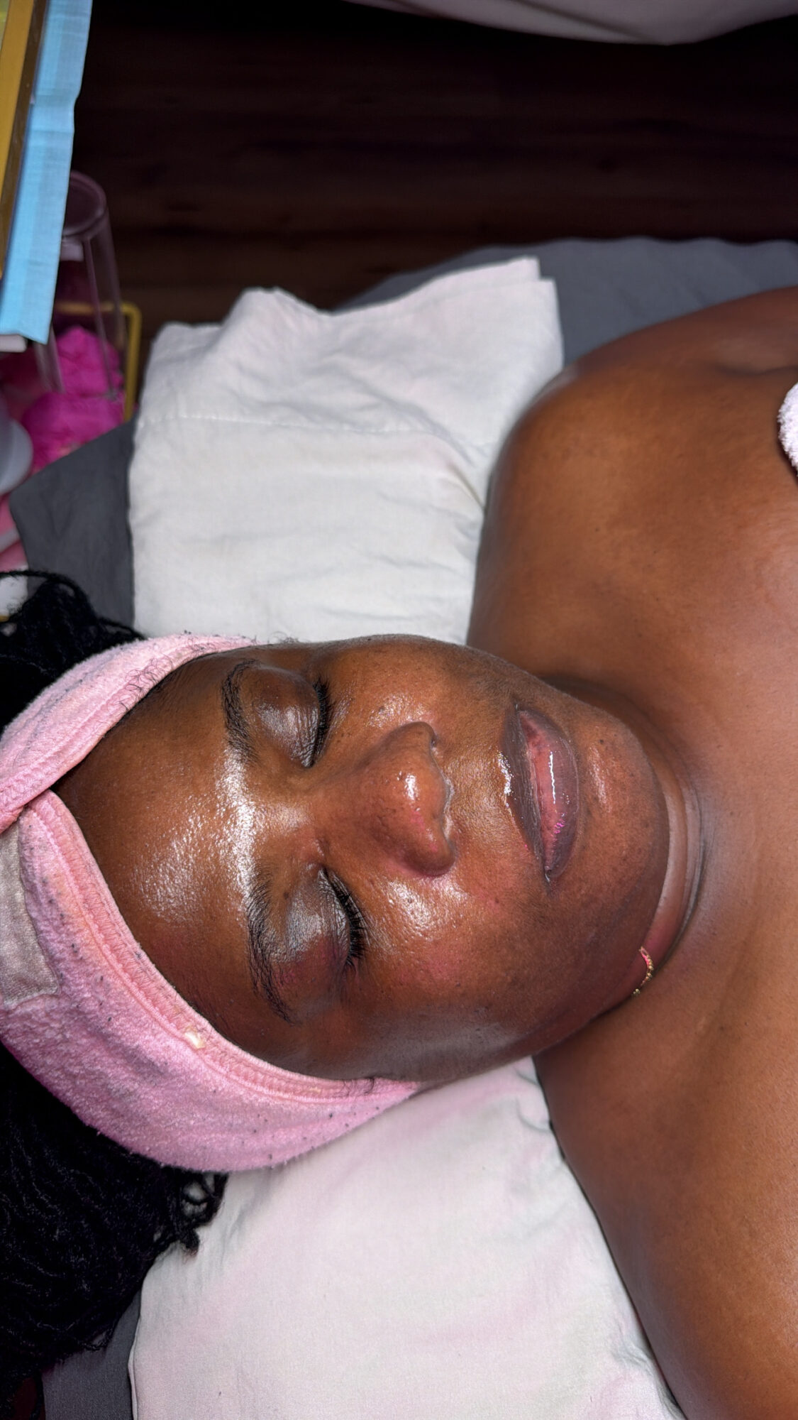 Woman lying with eyes closed, head wrapped in pink towel, on a white pillow.
