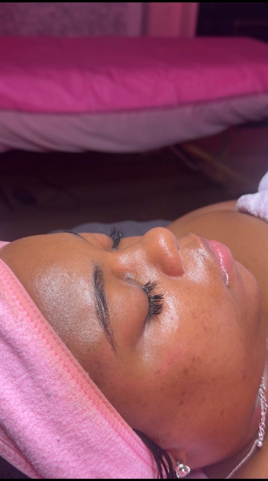 Close-up of a woman with eyes closed, lying down with a pink towel wrapped around her head.