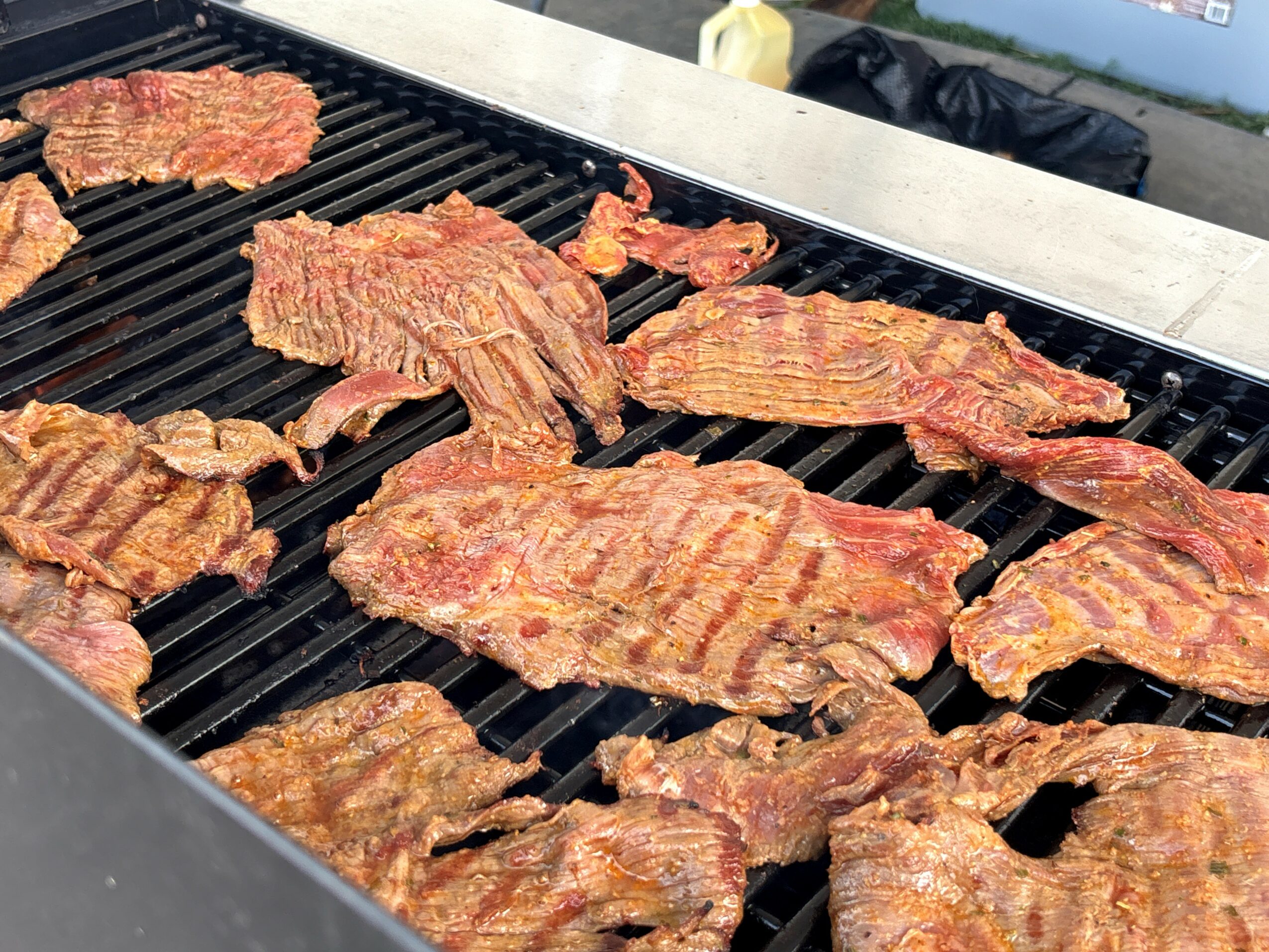 Several pieces of meat grilling on a barbecue with a scenic background, sunny weather, and a clear sky.