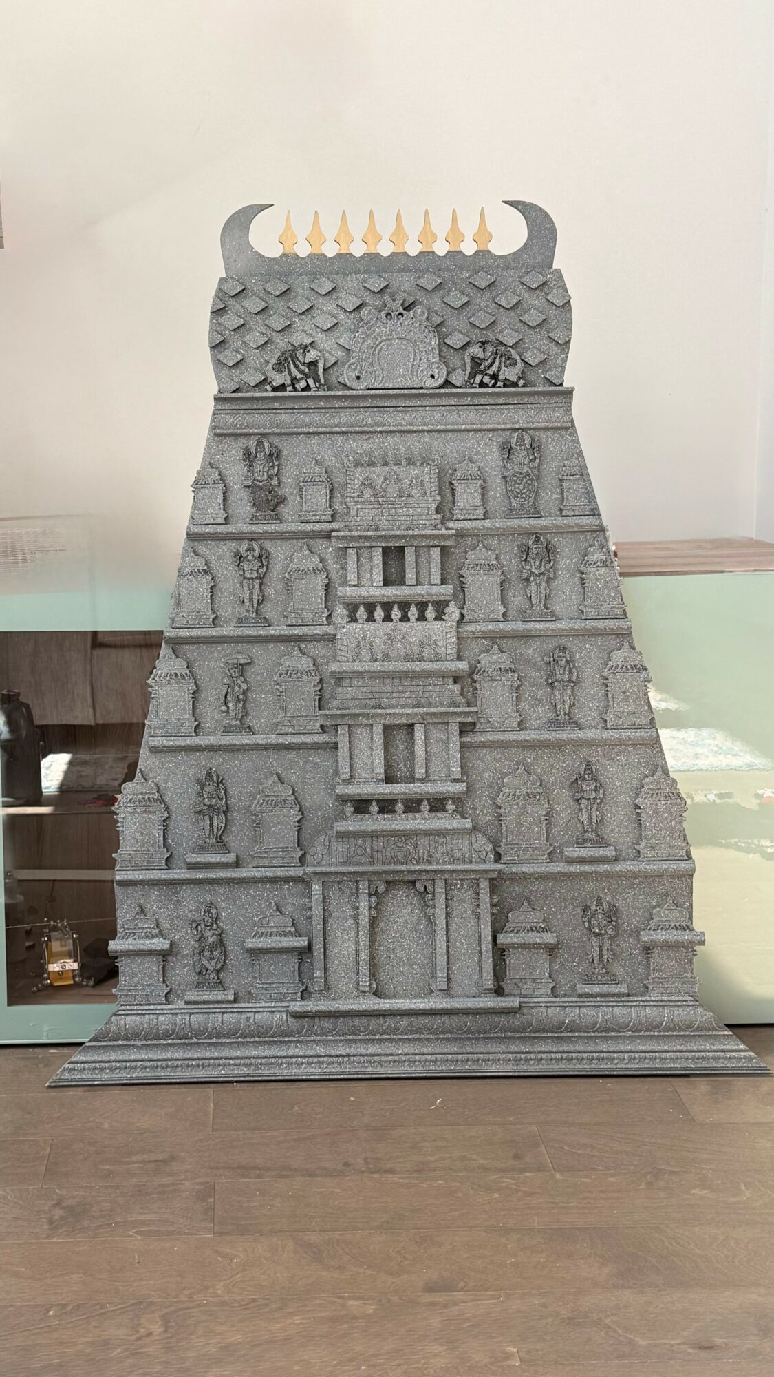 Gray stone temple with multiple levels, intricate carvings, and a row of golden ornaments at the top.