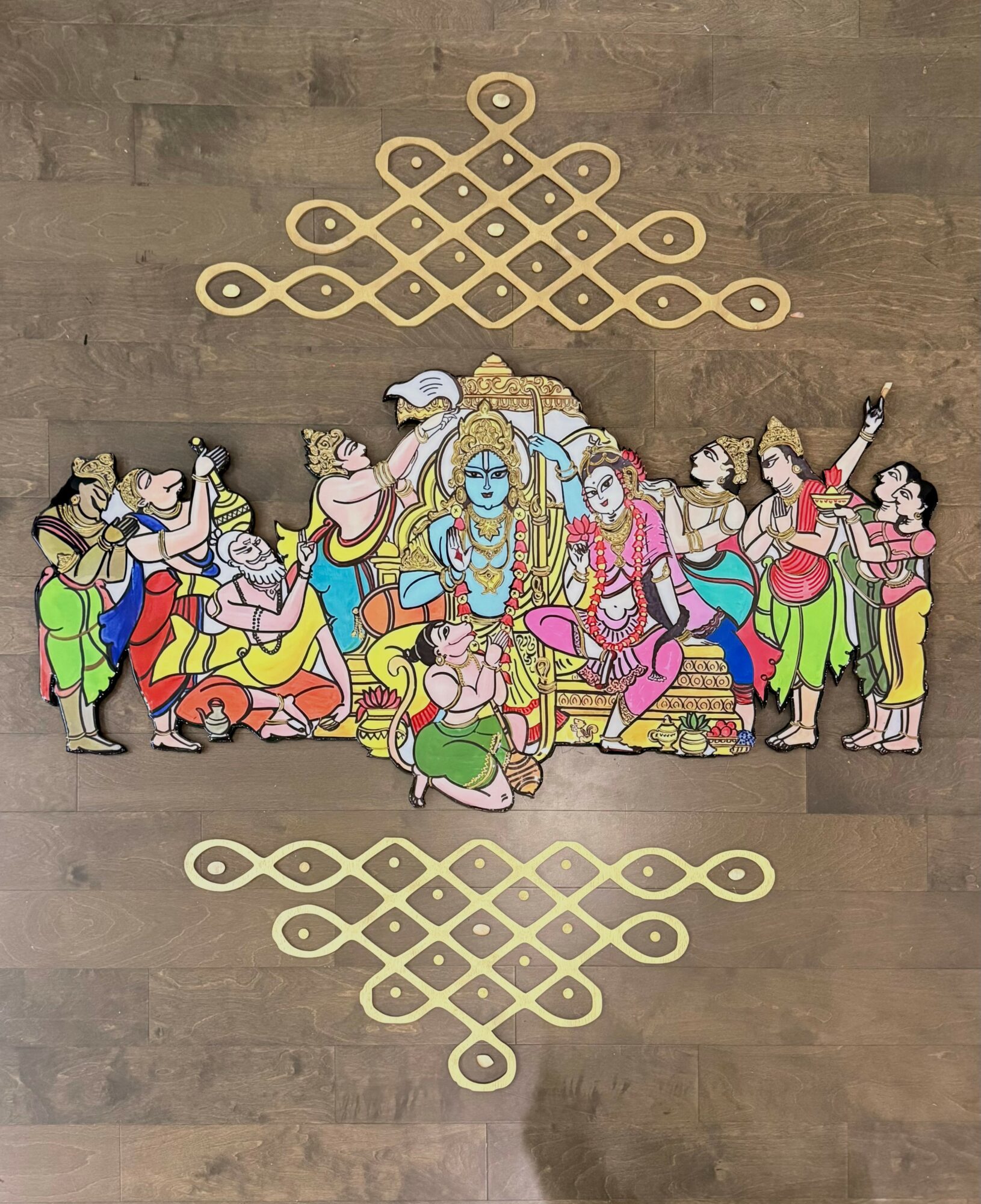Colorful illustration of a central figure surrounded by people, with decorative patterns above and below, on a wooden background.