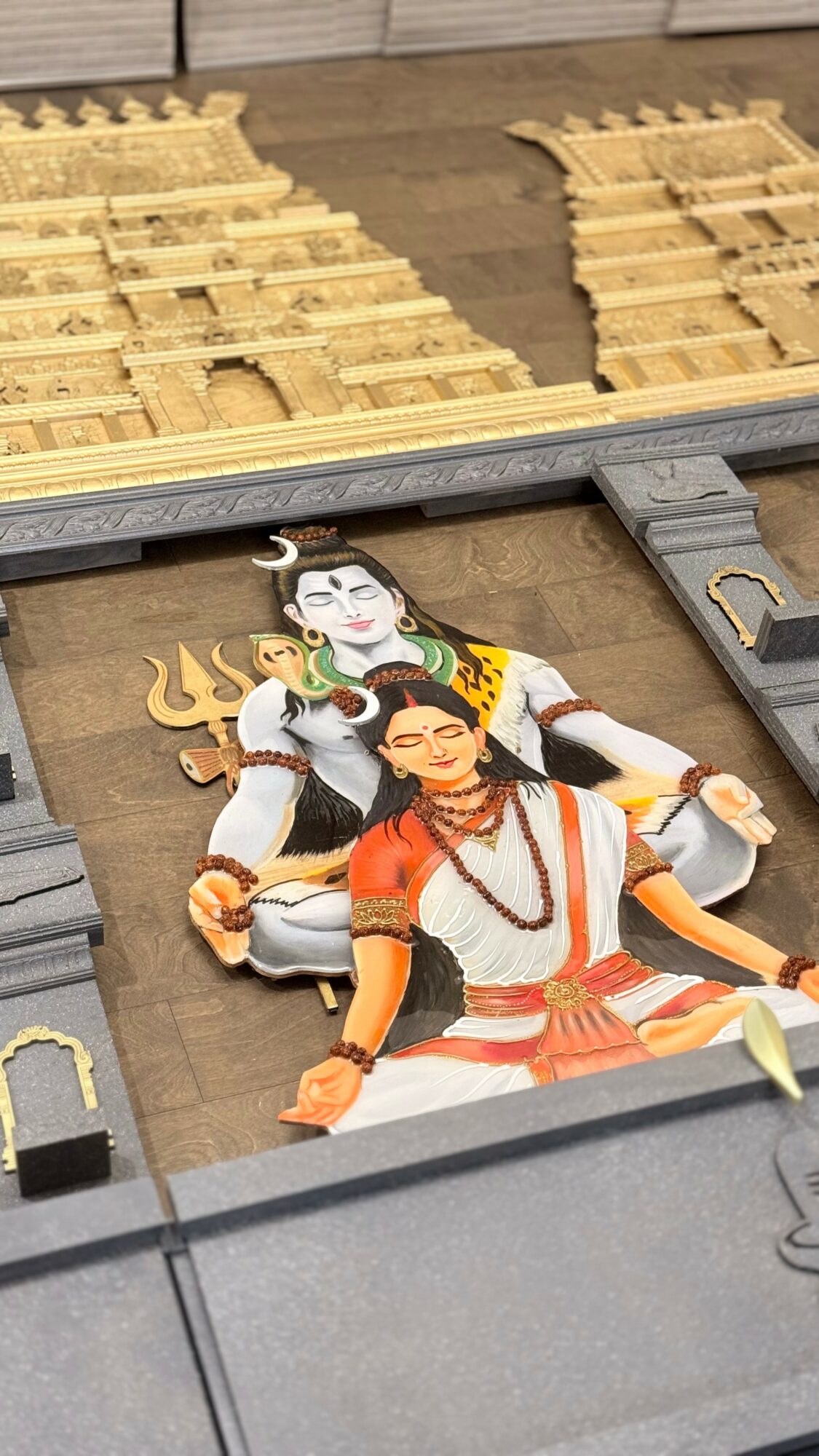 Colorful statue of two figures in traditional attire inside a gray structure, with wooden pallets in the background.