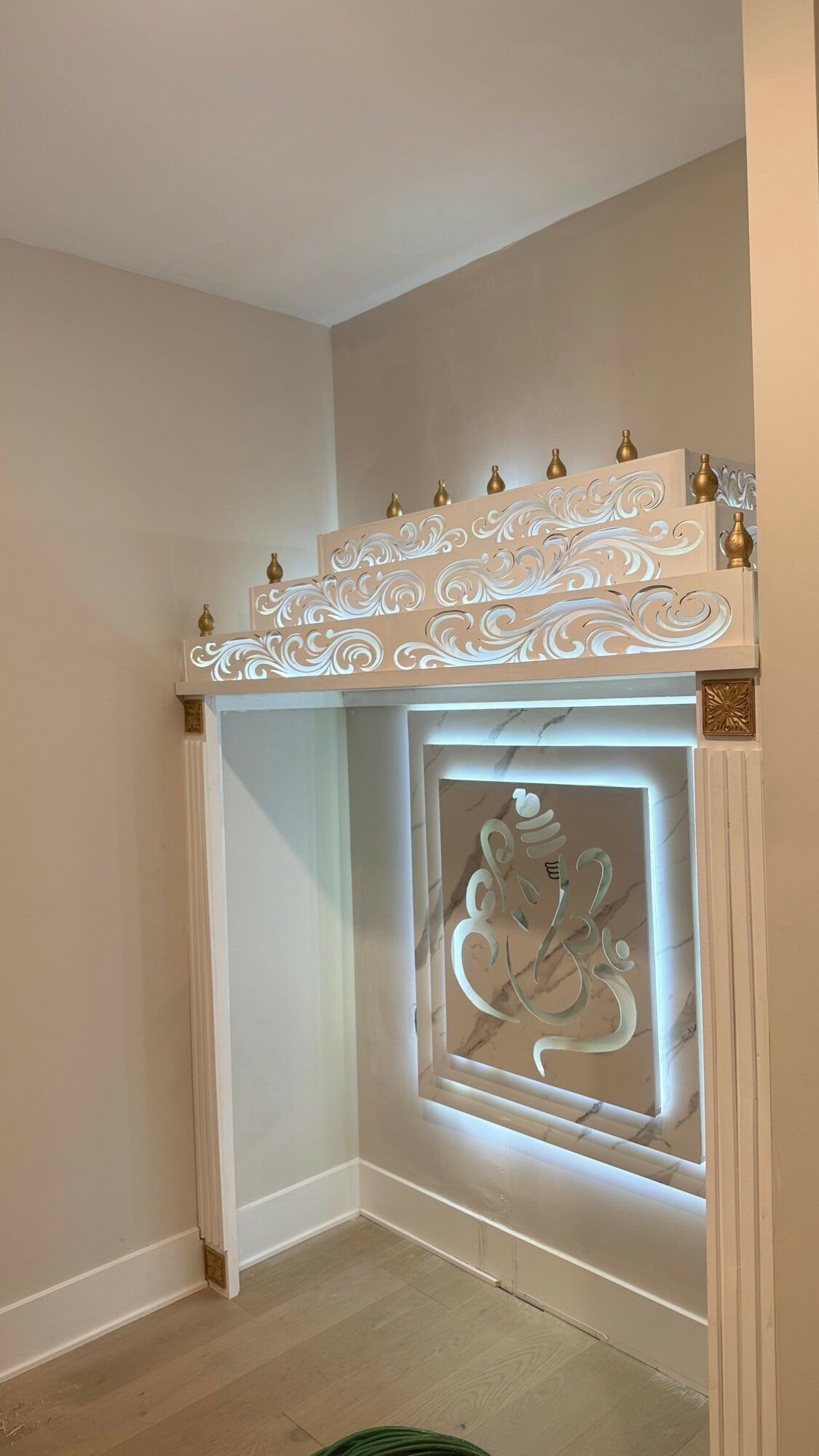 Decorative window with ornate white trim and a carved design, set in a beige wall with a light-colored floor.