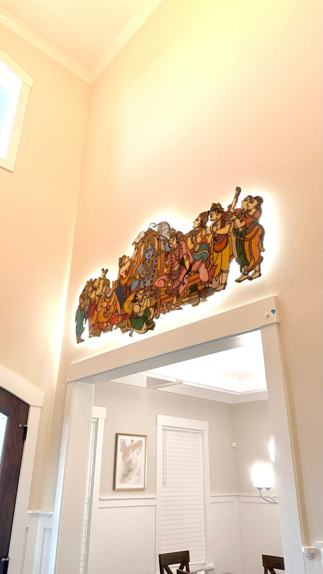 Colorful religious or cultural artwork on a wall above a doorway, with a window and framed picture in the background.