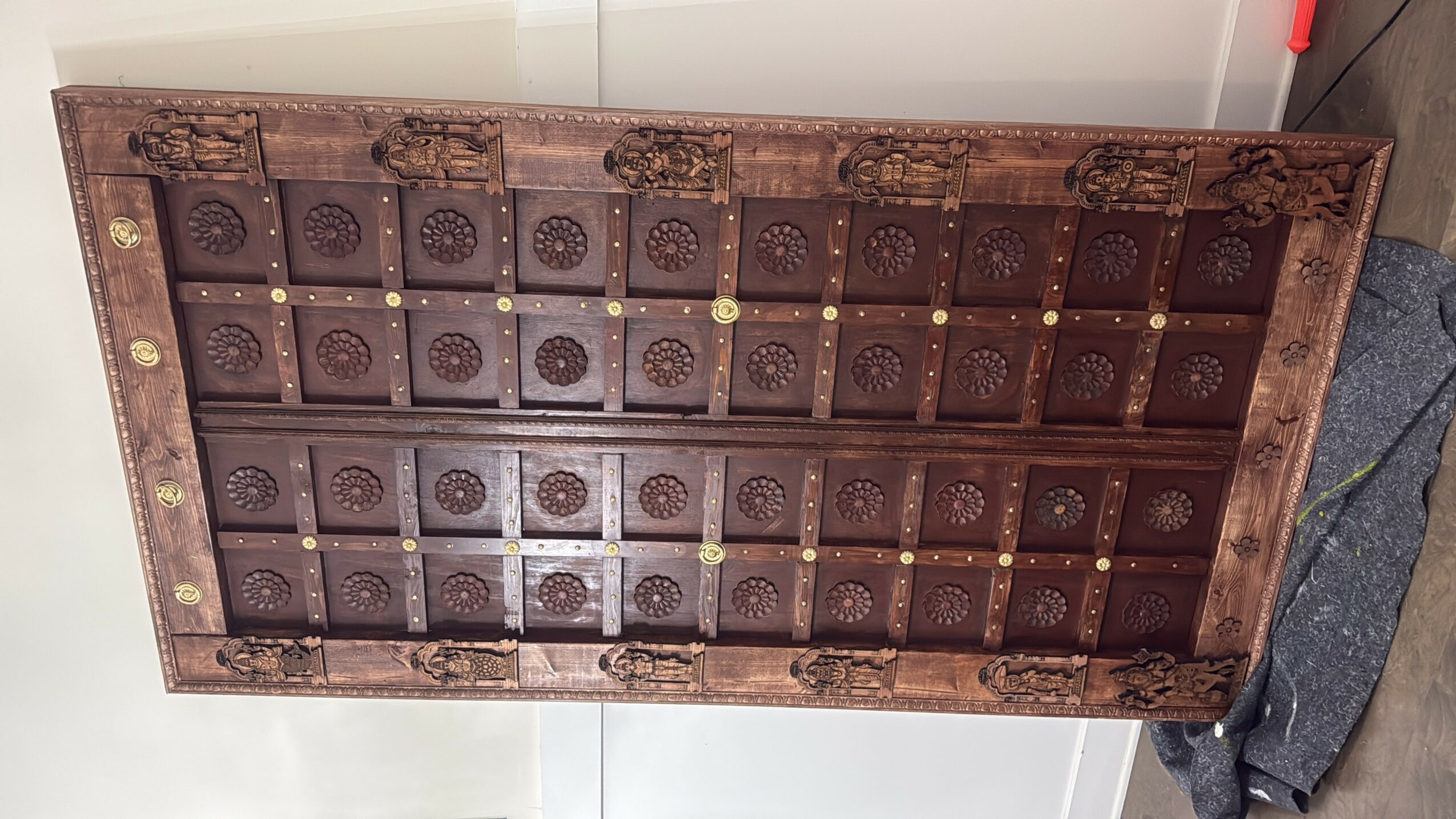 Wooden chessboard with carved squares and decorative border, placed on a surface with a gray cloth nearby.