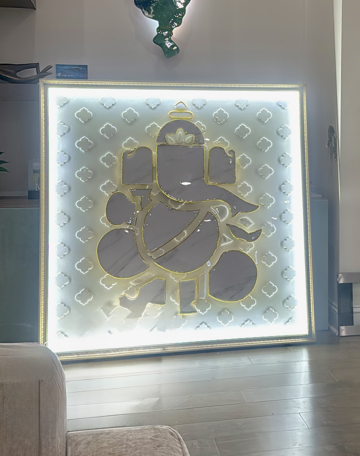 Backlit artwork of Lord Ganesha with a decorative background, placed indoors on a wooden floor.