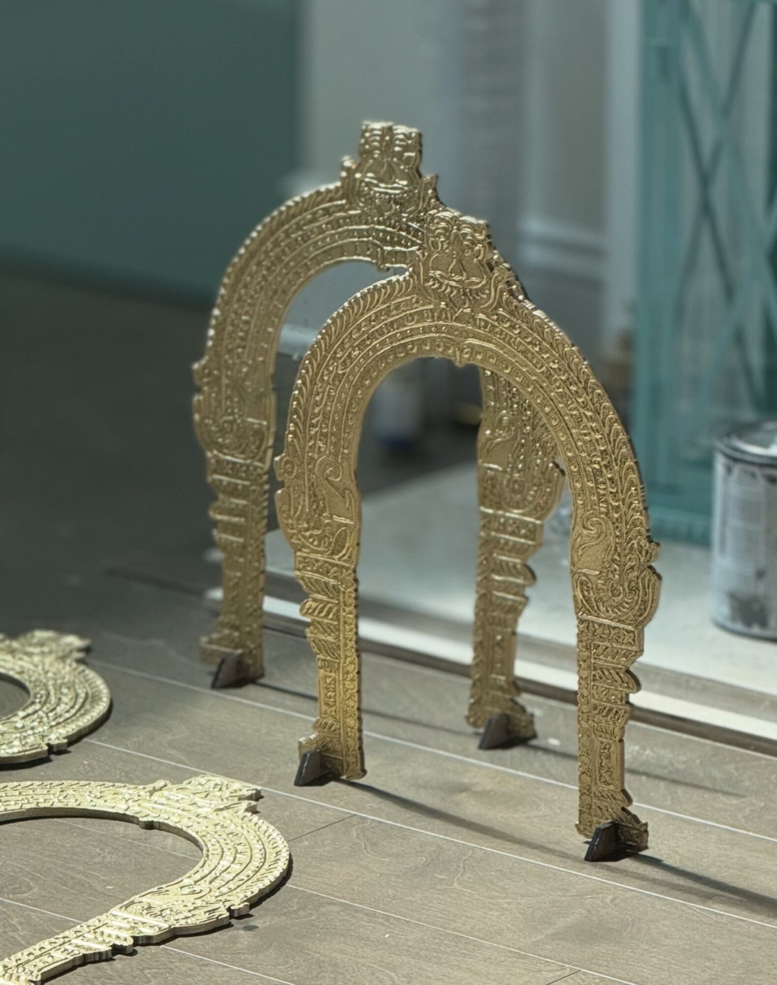 Two ornate gold arch-shaped objects with intricate designs, standing on a surface near a mirror and other decorative items.