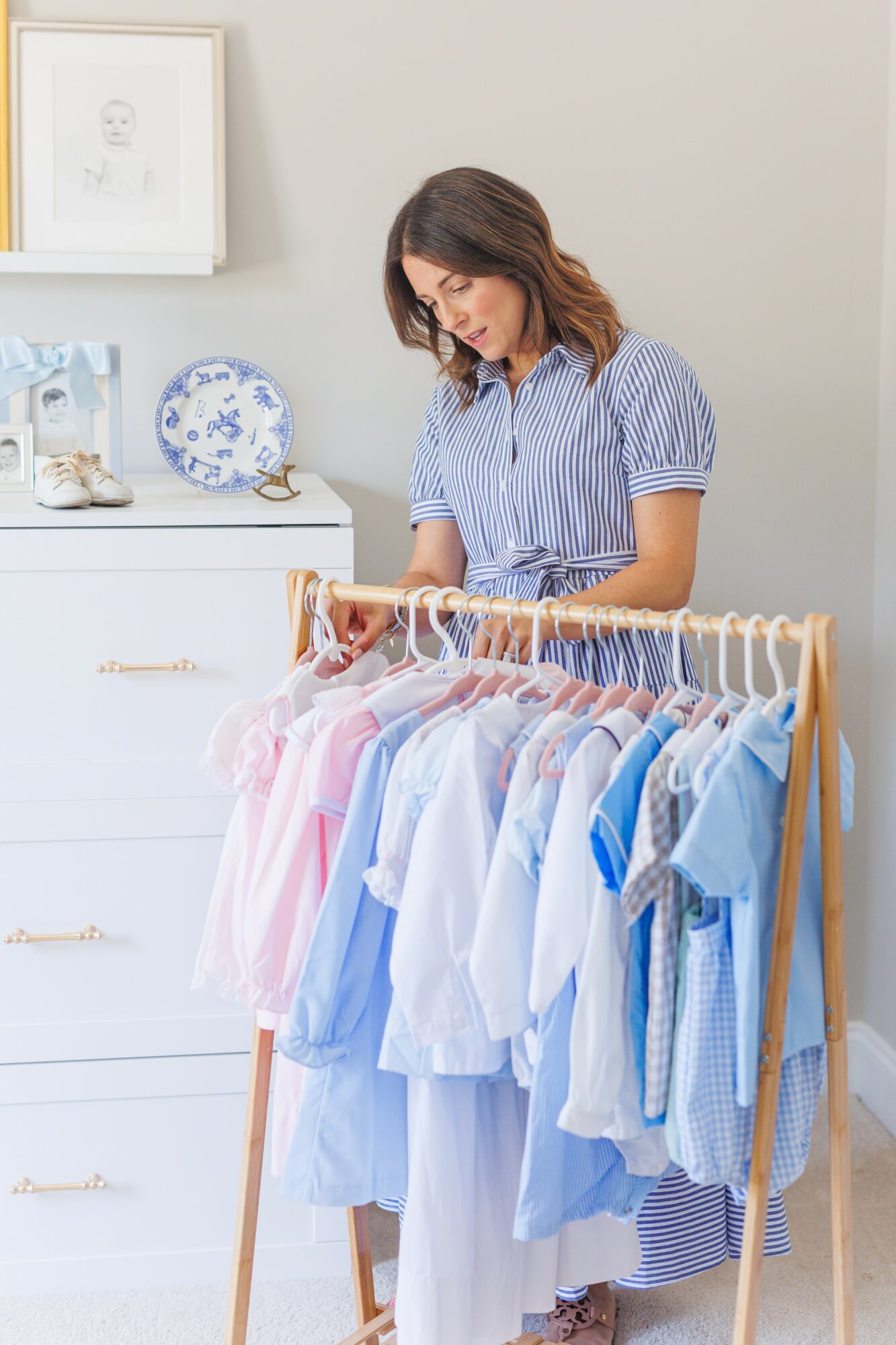 Woman browsing clothes on a rack in a bright room with white furniture and decorative items.