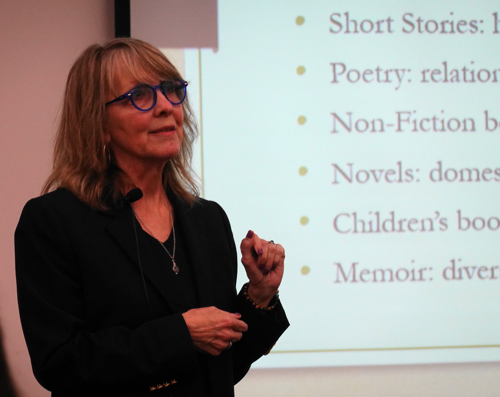 Woman with glasses and shoulder-length hair giving a presentation in front of a screen with text.