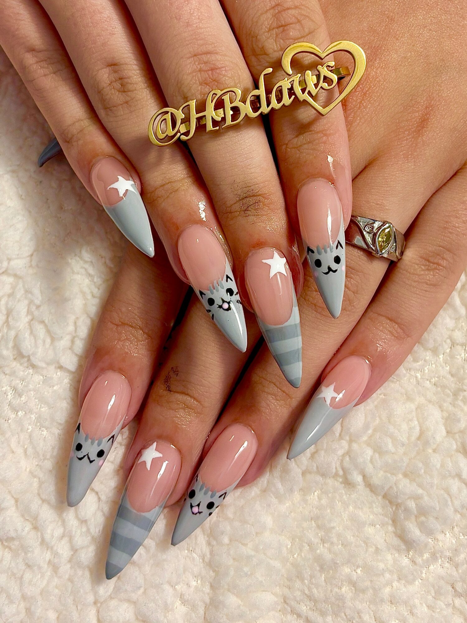Close-up of hands with decorated nails, featuring gray and white striped patterns, stars, and panda faces, on a soft surface.