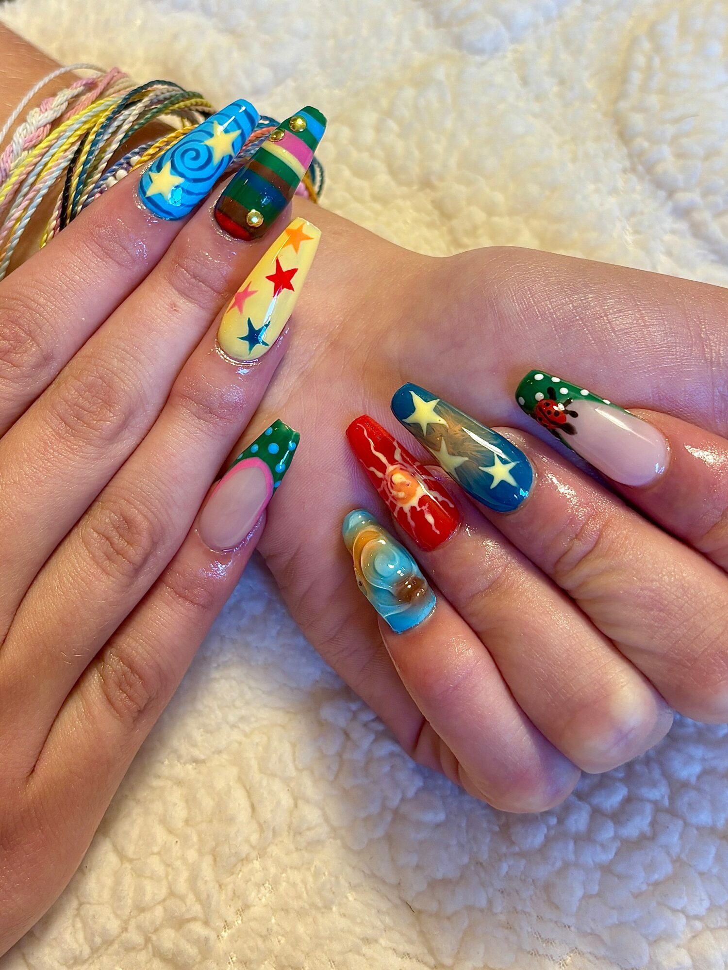 Hands with colorful, star-themed nail art, decorated with various bright colors and patterns, resting on a soft, cream-colored surface.