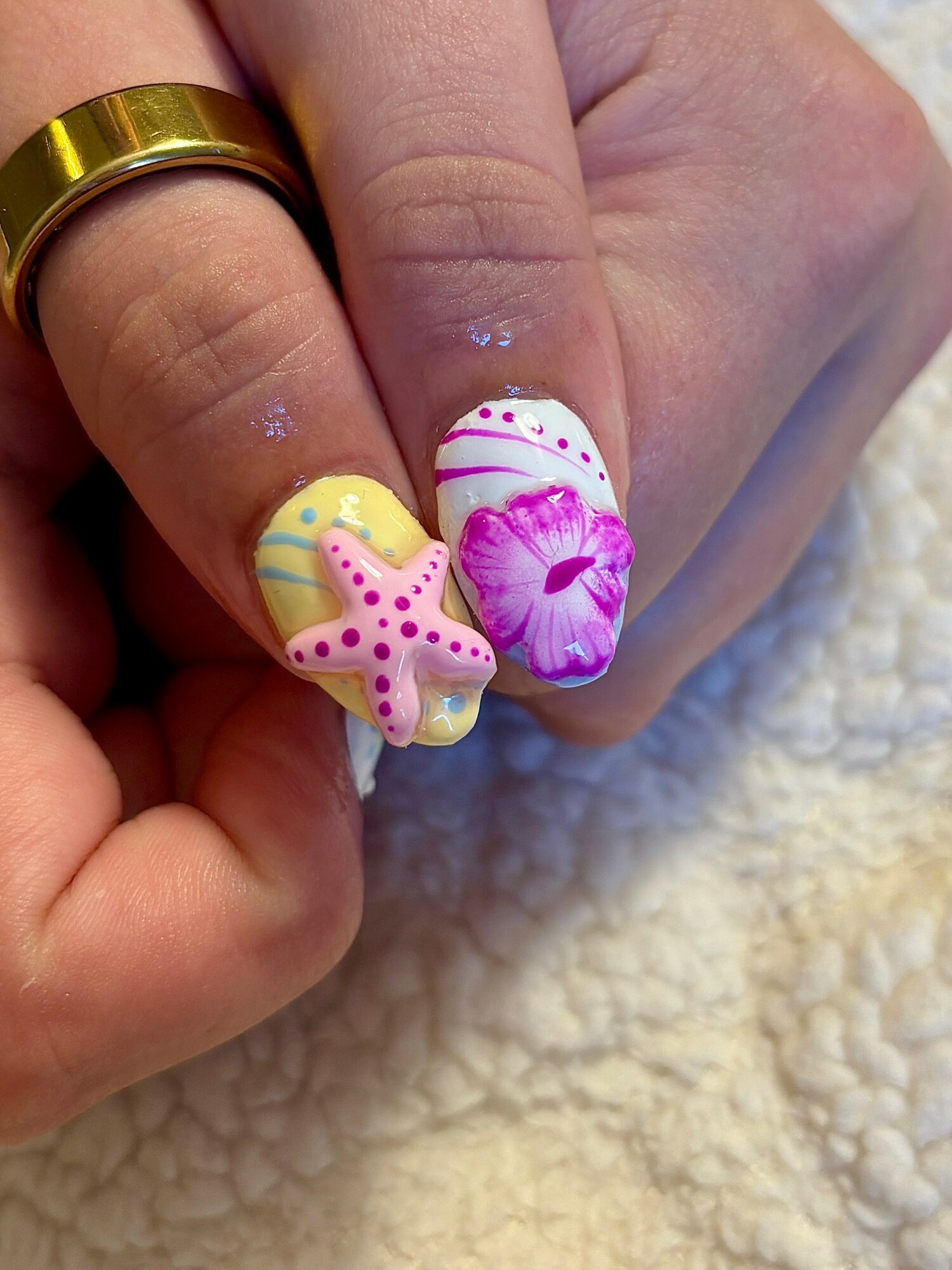 Close-up of a hand with decorated nails featuring pastel colors, a starfish, and seashell designs, on a soft surface.