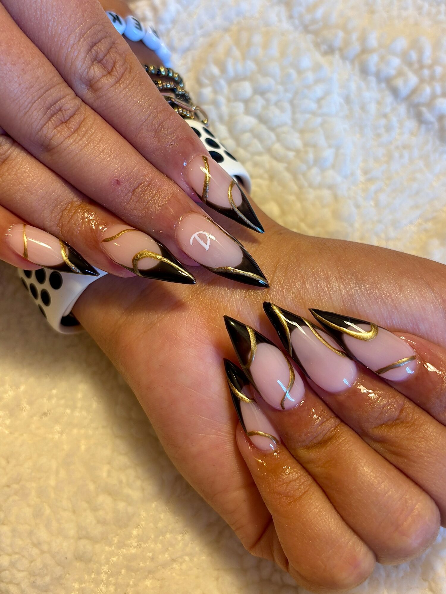 Close-up of hands with long, pointed nails featuring black, white, and gold designs, resting on a textured surface.