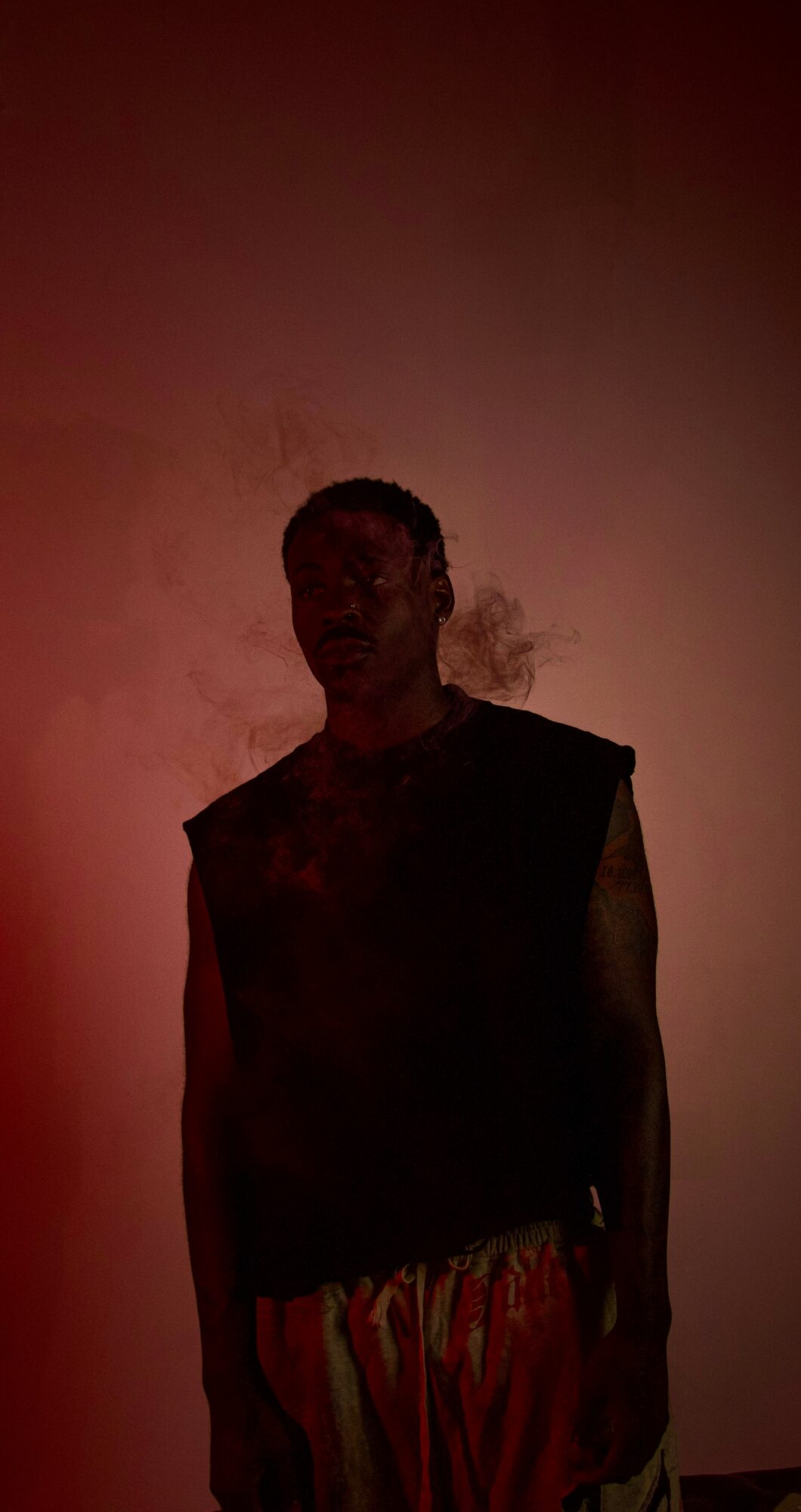 Silhouette of a person standing against a reddish background with smoke or mist nearby.
