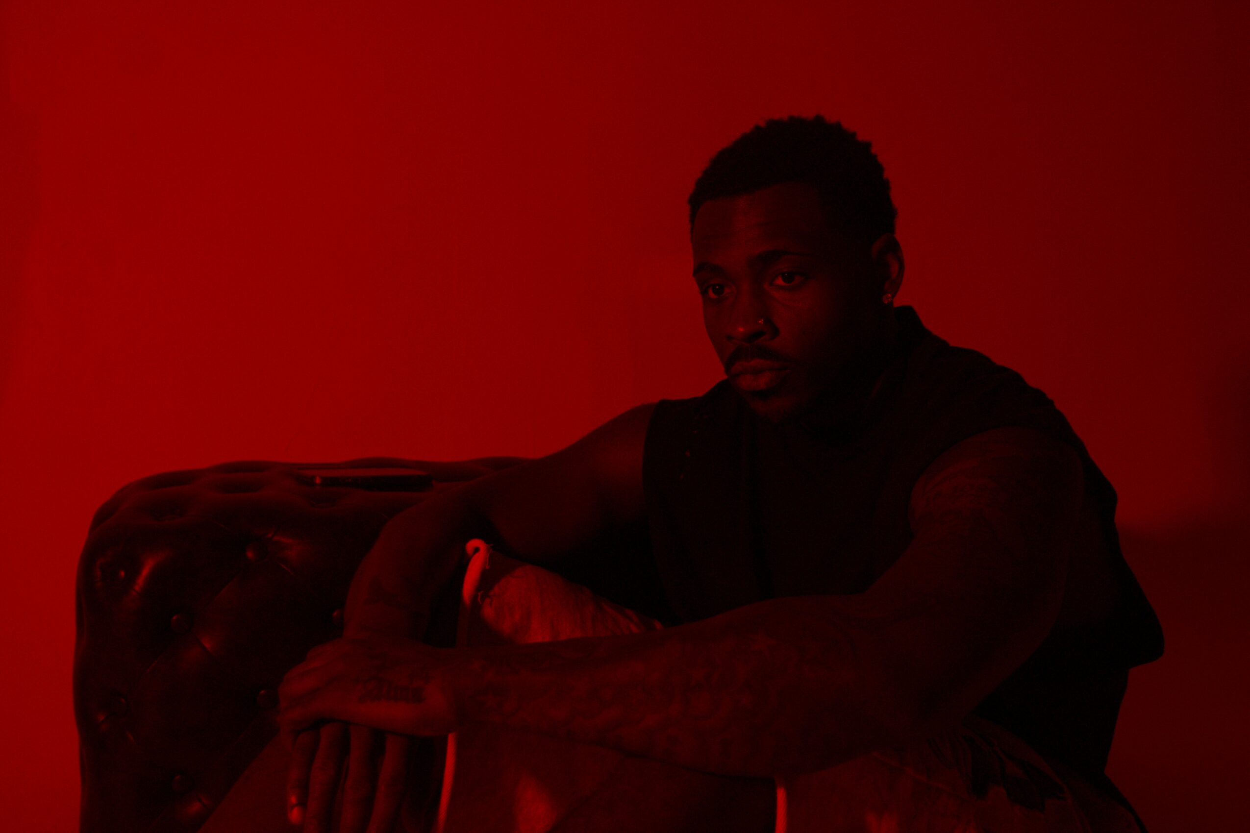 Person sitting on a couch with a red background, arms crossed, looking at the camera.